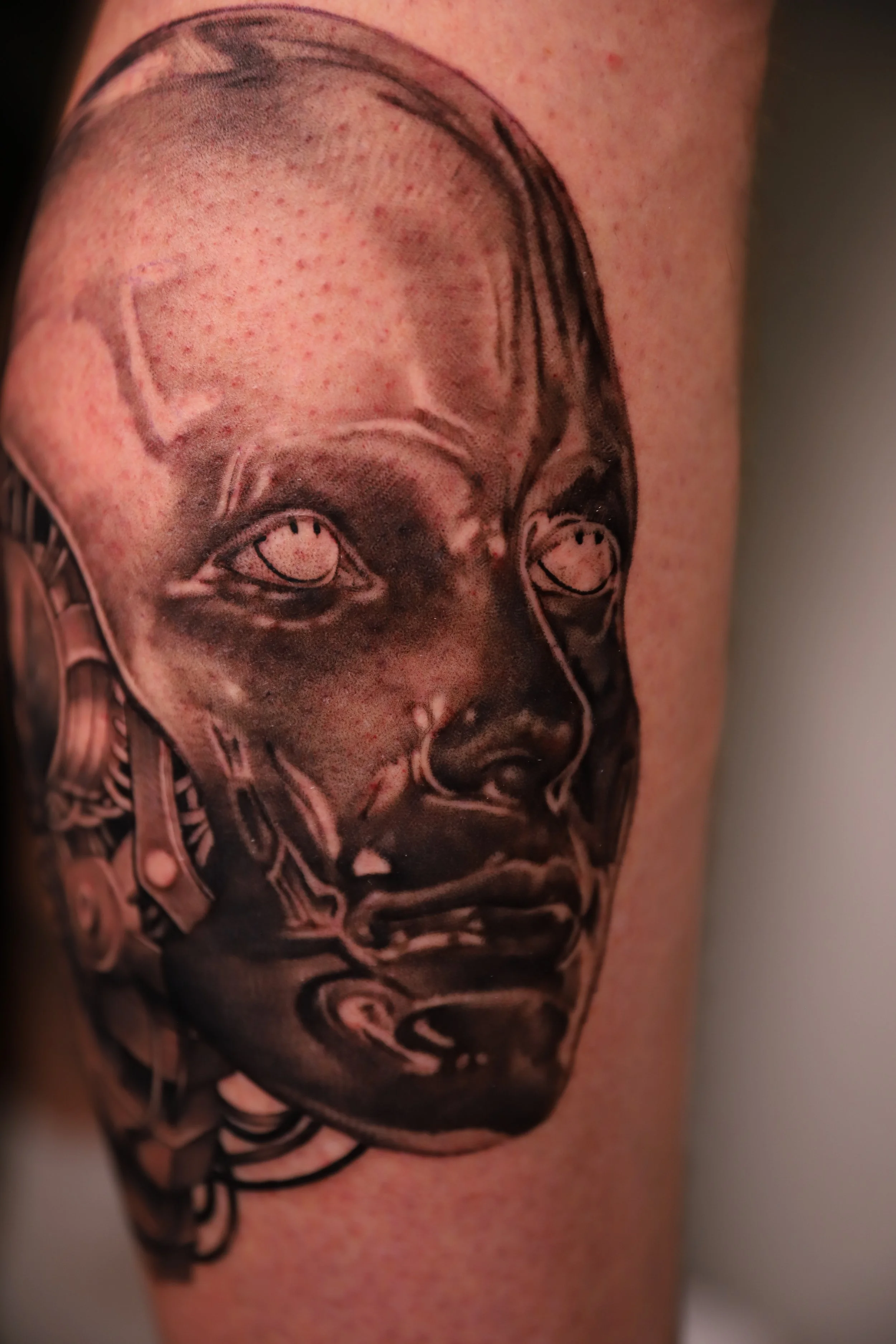 Close-up of a black and grey tattoo of a person's face on skin.
