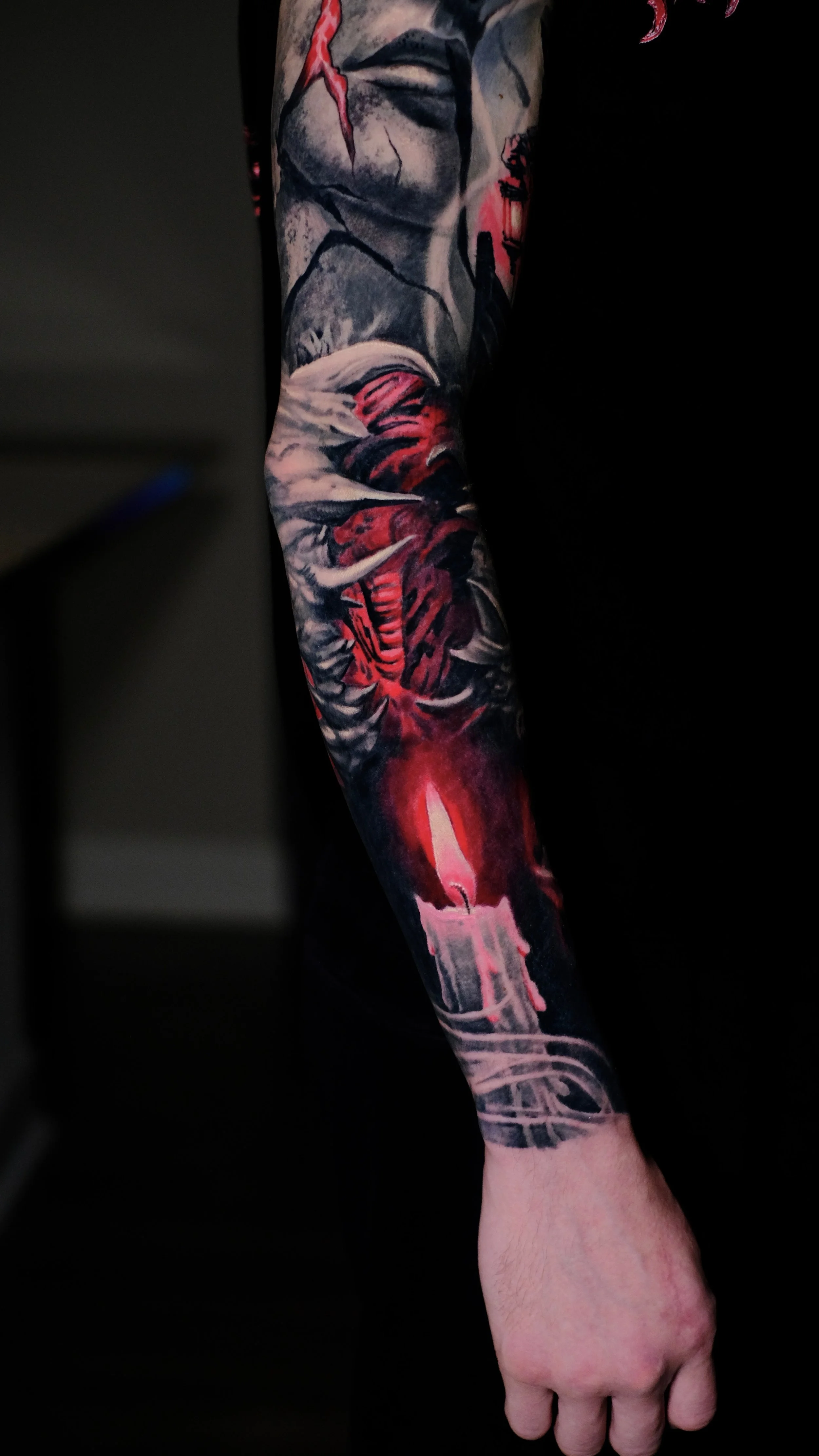 Tattoo of a woman's face on the upper arm with cracked skin and a red lightning bolt, along with a red and black skull on the forearm.