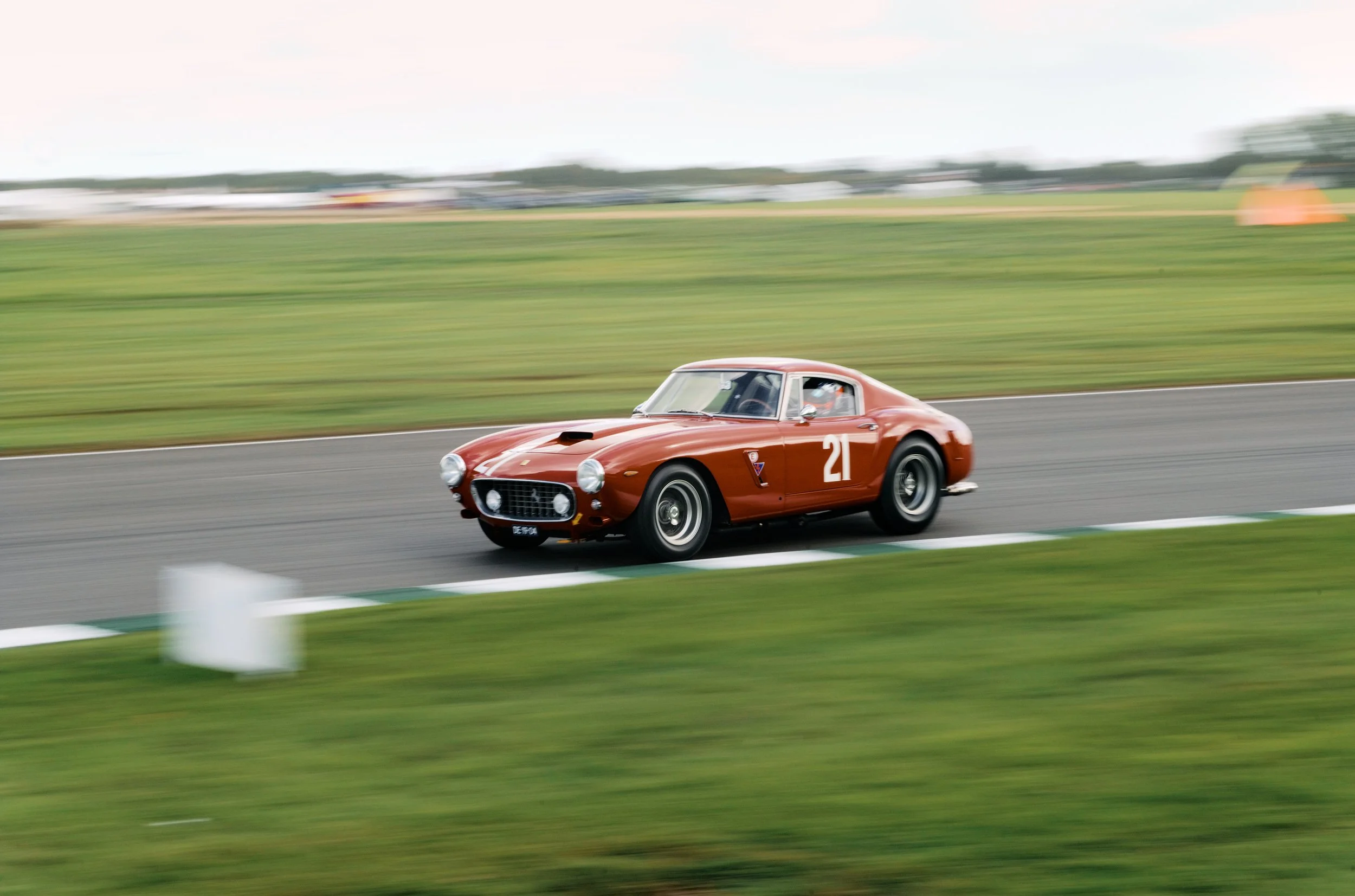 A vintage red race car with the number 21 on its side speeding on a racetrack, with a blurred background indicating motion.