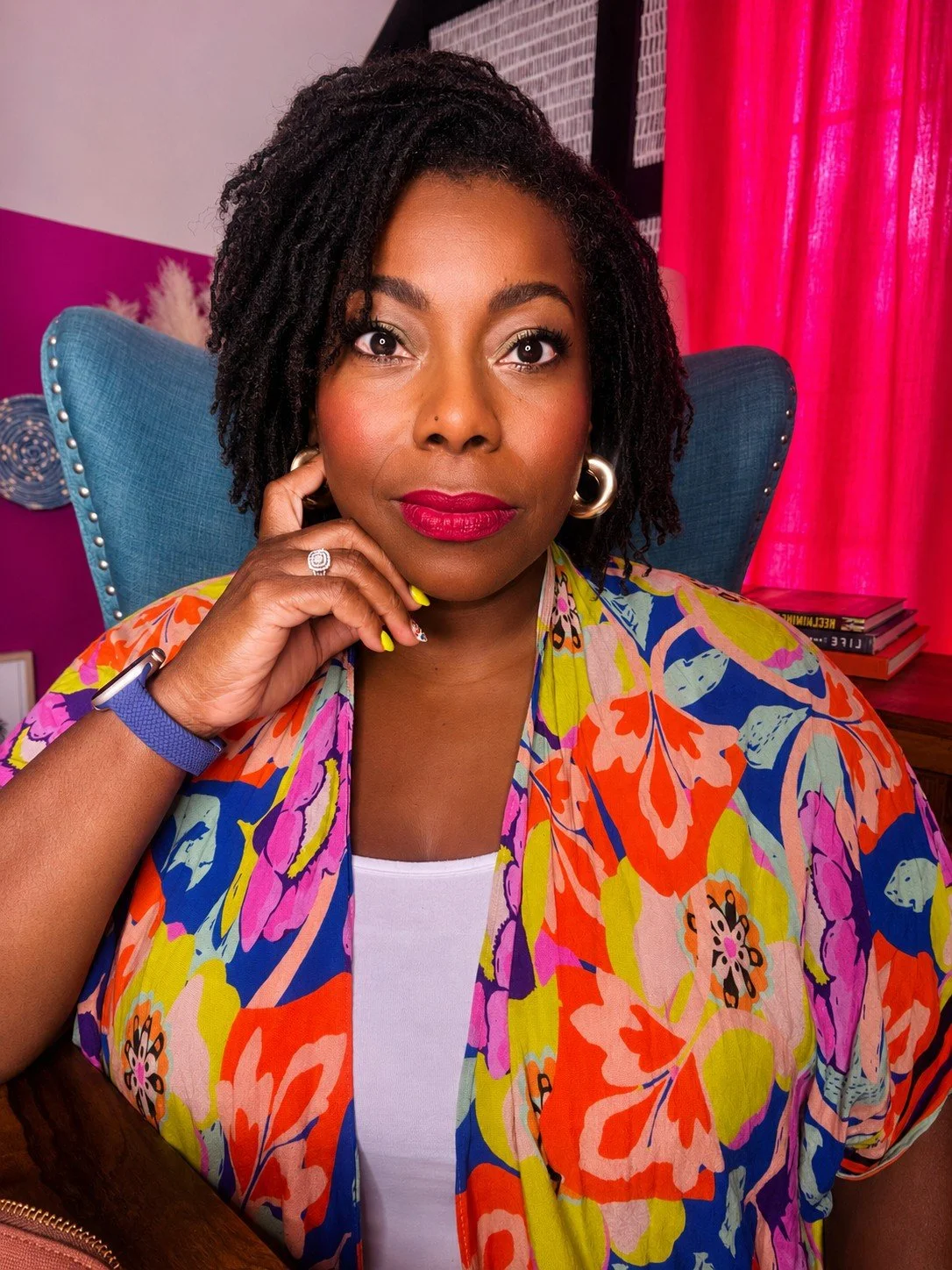 Picture of Brigida Mack, a Black woman with locs wearing a flowered print kimono with a warm but serious expression.