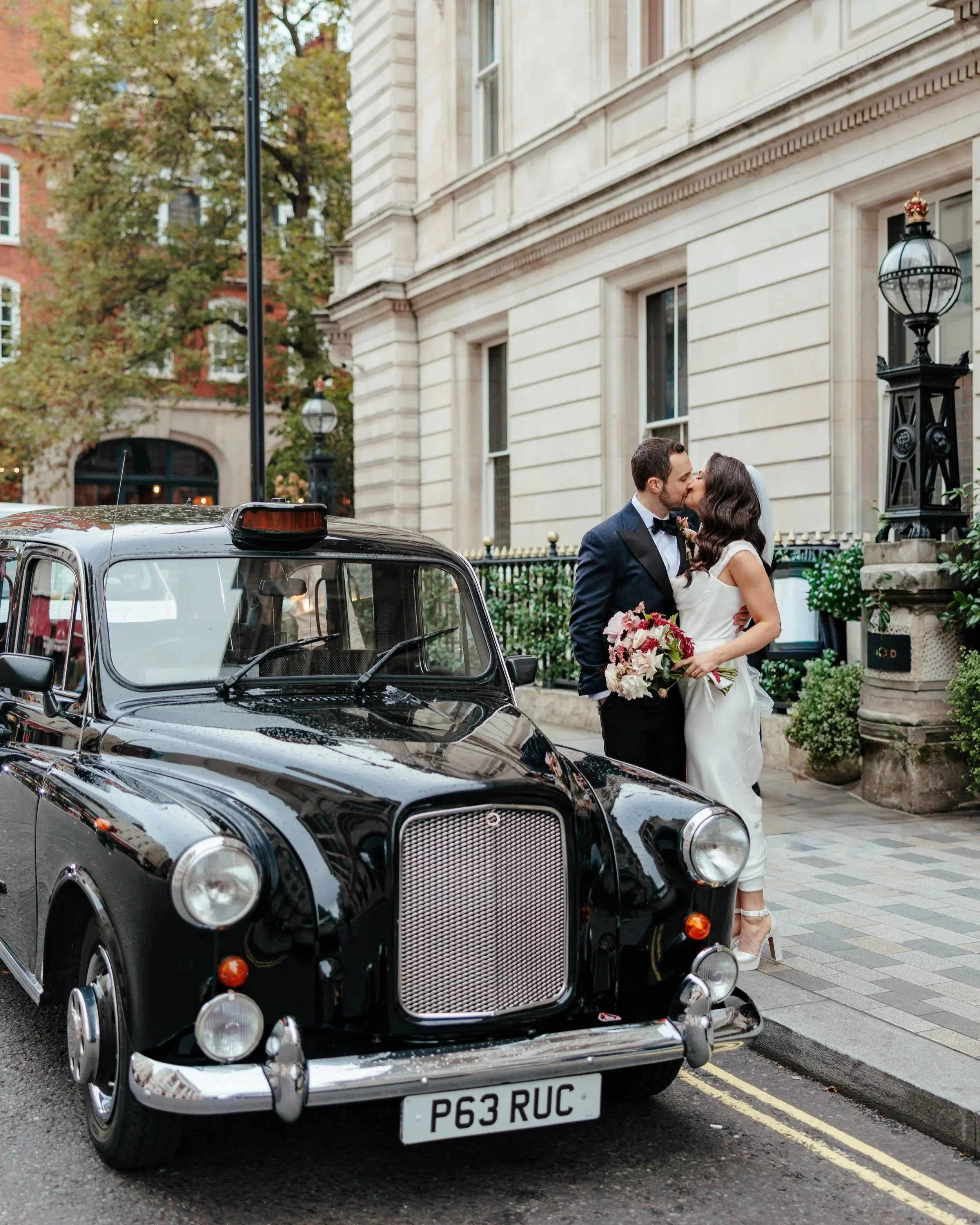 Bride and groom kissing beside vintage London black cab on wedding day