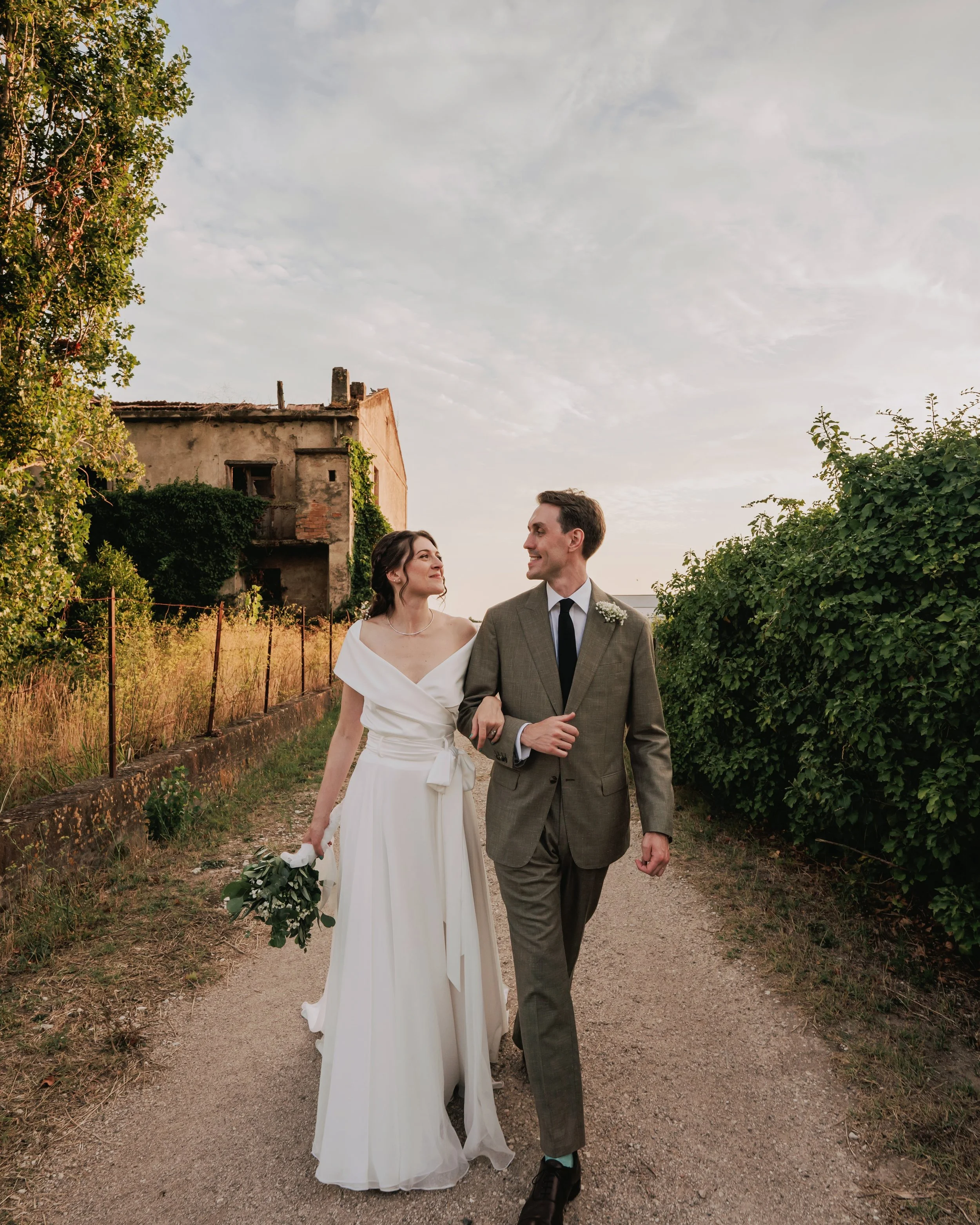 A groom and his bride walking in arm in arm after their destination wedding in Italy, the groom wearing a bespoke wedding suit made by bespoke tailor Roberto Revilla London