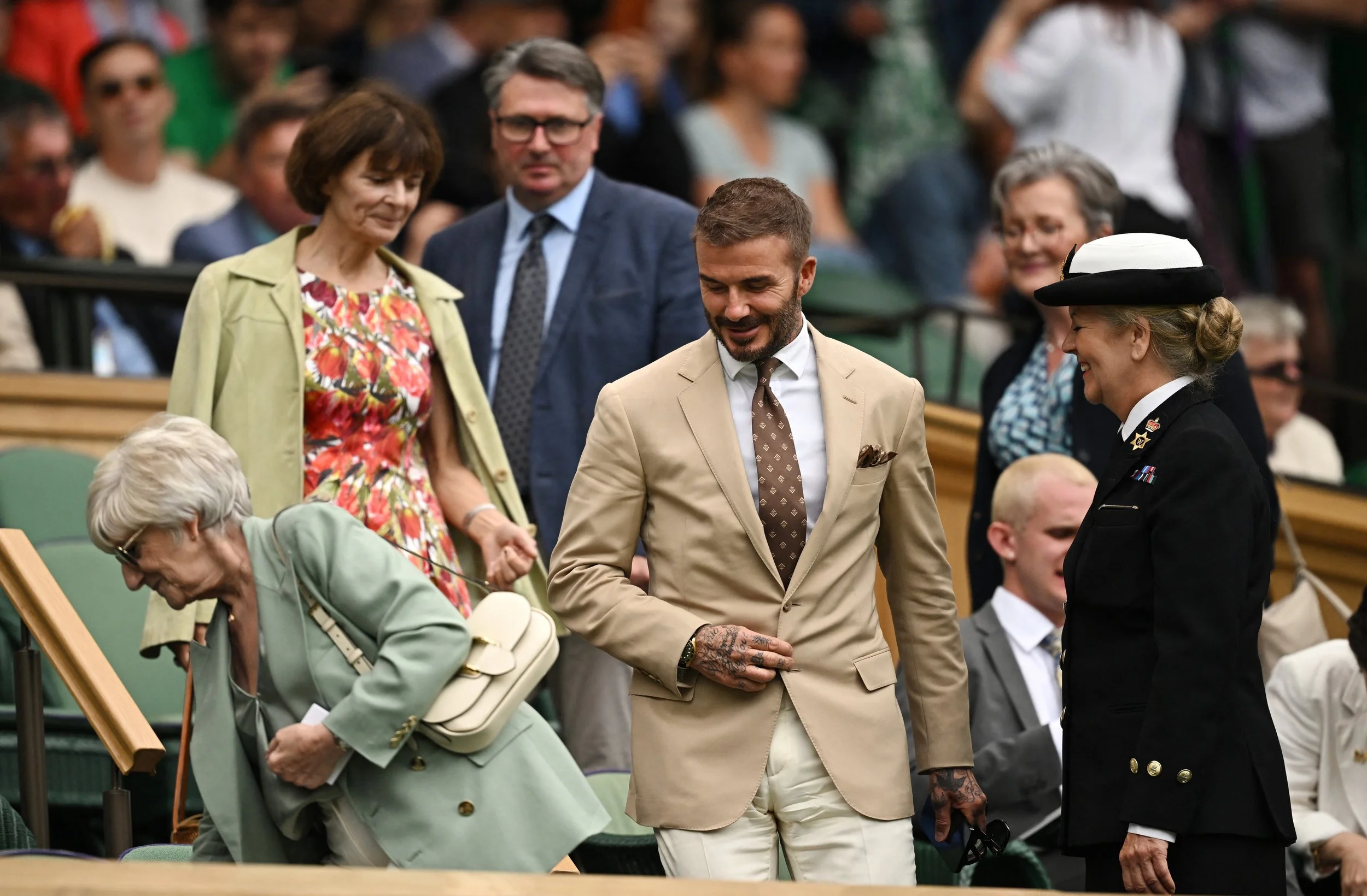David Beckham at Wimbledon wearing a khaki blazer, brown patterned tie, white shirt and creme trousers