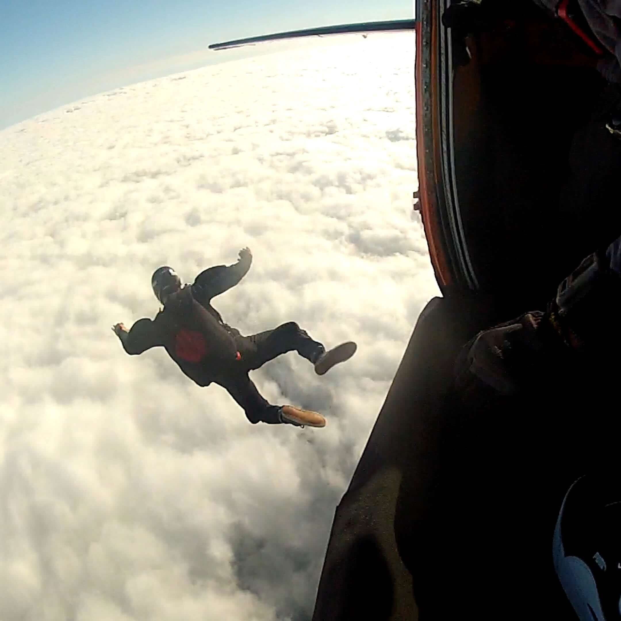  Chris jumping out of a plane above the clouds wearing a parachute 
