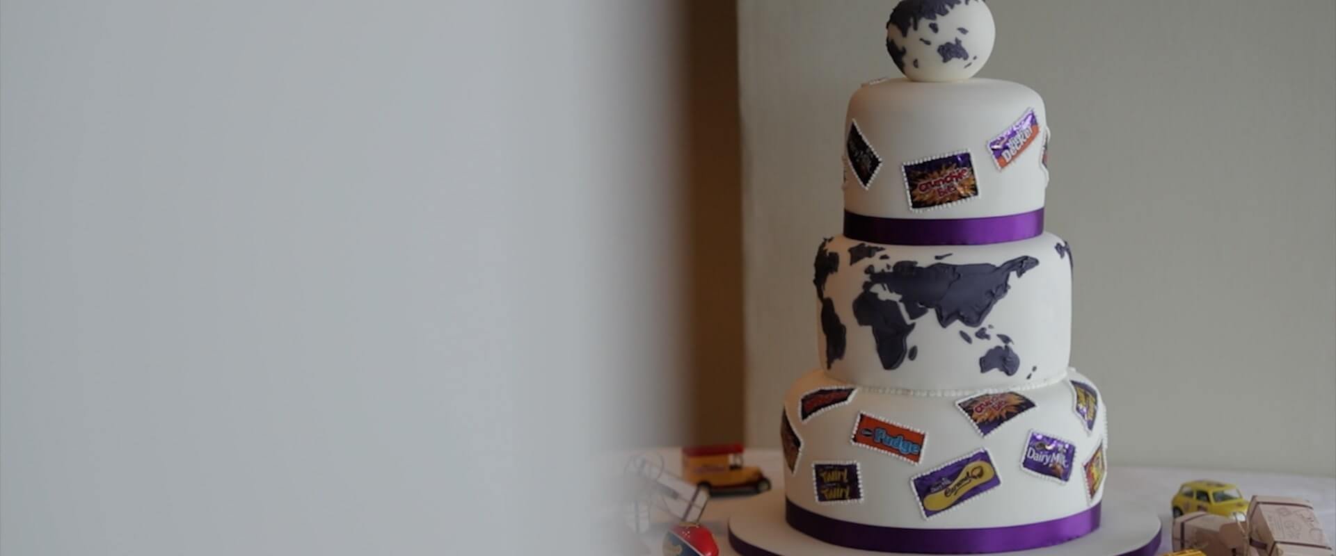 A closeup of a Cadbury's themed wedding cake, with famous cadbury's chocolate logos drawn on in icing