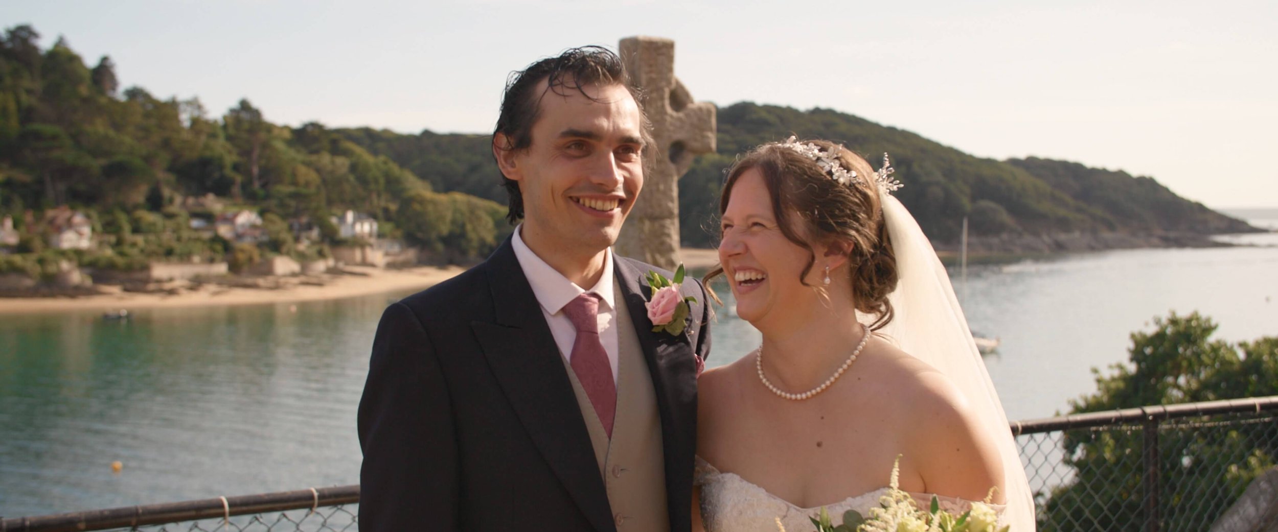 Stephen makes Amy laugh as they stand in front of the Salcombe Estuary in their wedding outfits