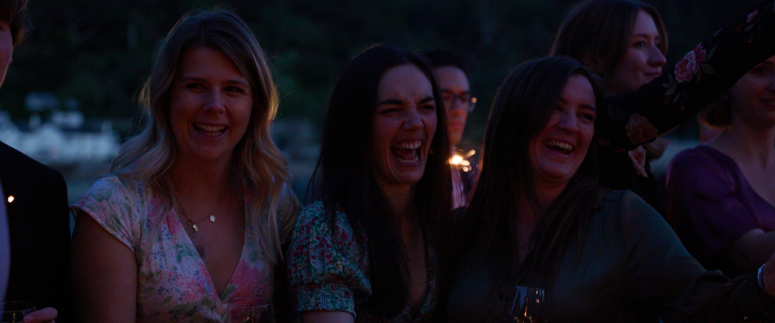3 female wedding guests laugh hysterically as they enjoy playing with sparklers