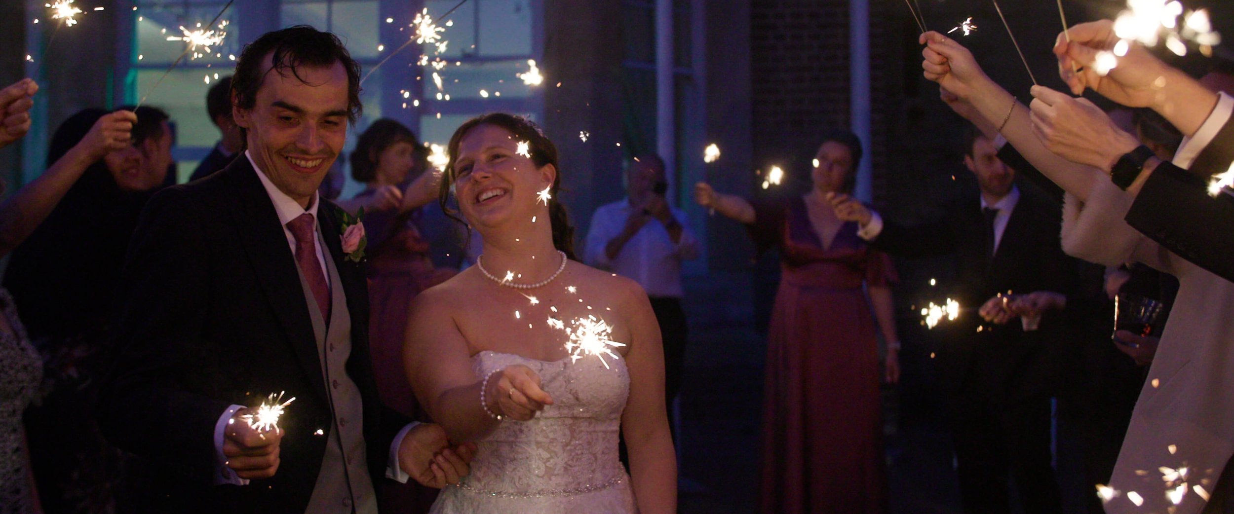 Amy &amp; Stephen joyfully play with sparklers surrounded by their wedding guests