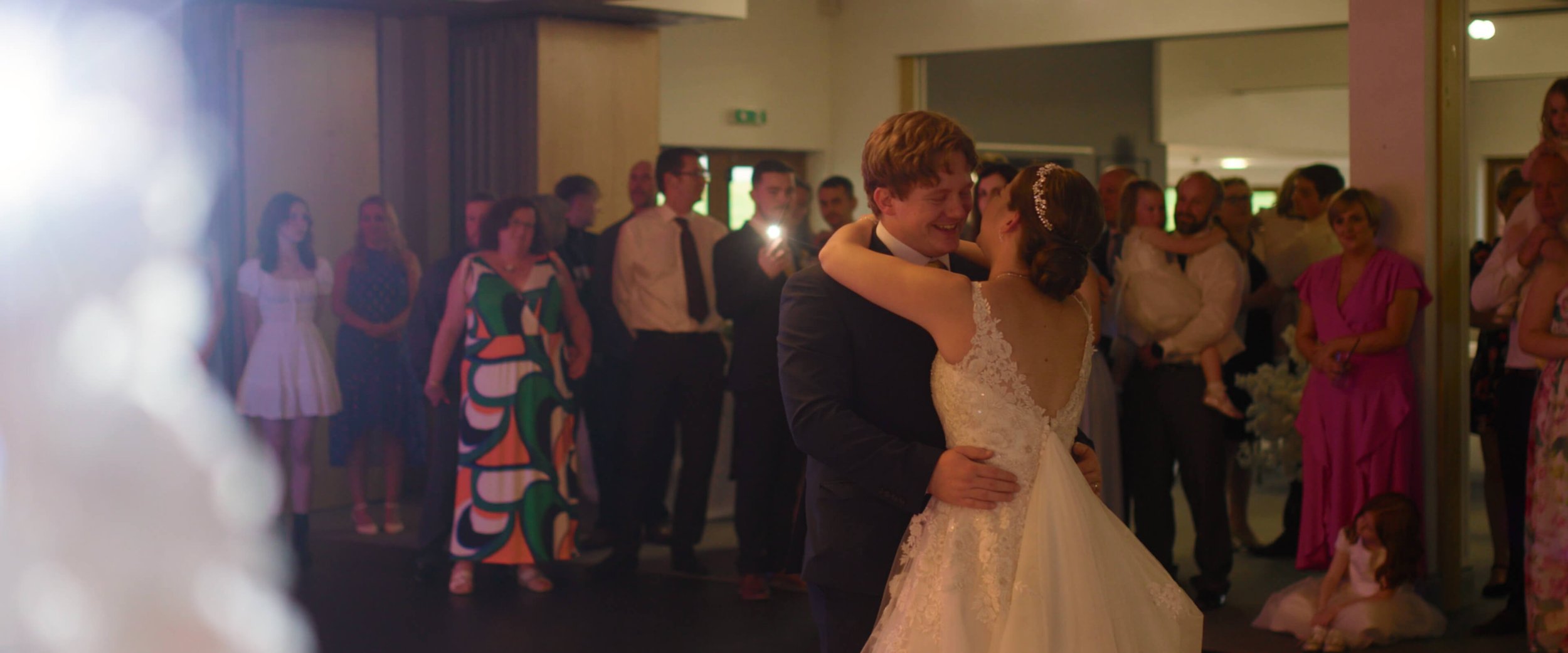 Dael &amp; Emma holding each other during the first wedding dance as the guests watch and film on their phones