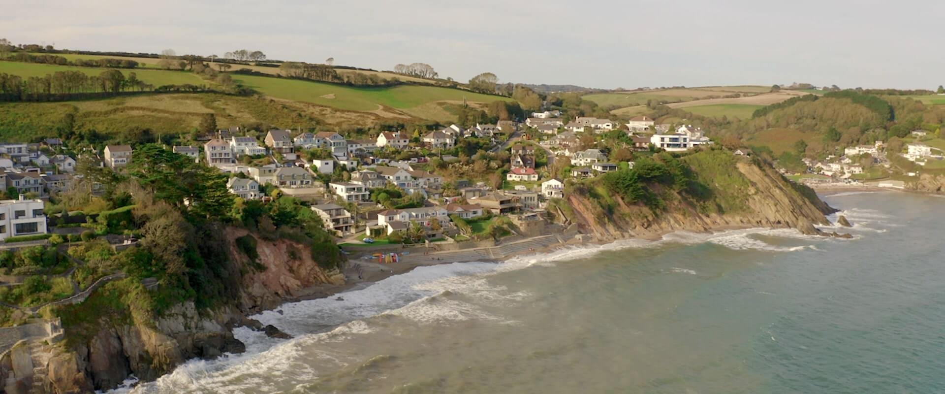 An aerial drone shot of the waves crashing into the cliffs surround Looe Estuary