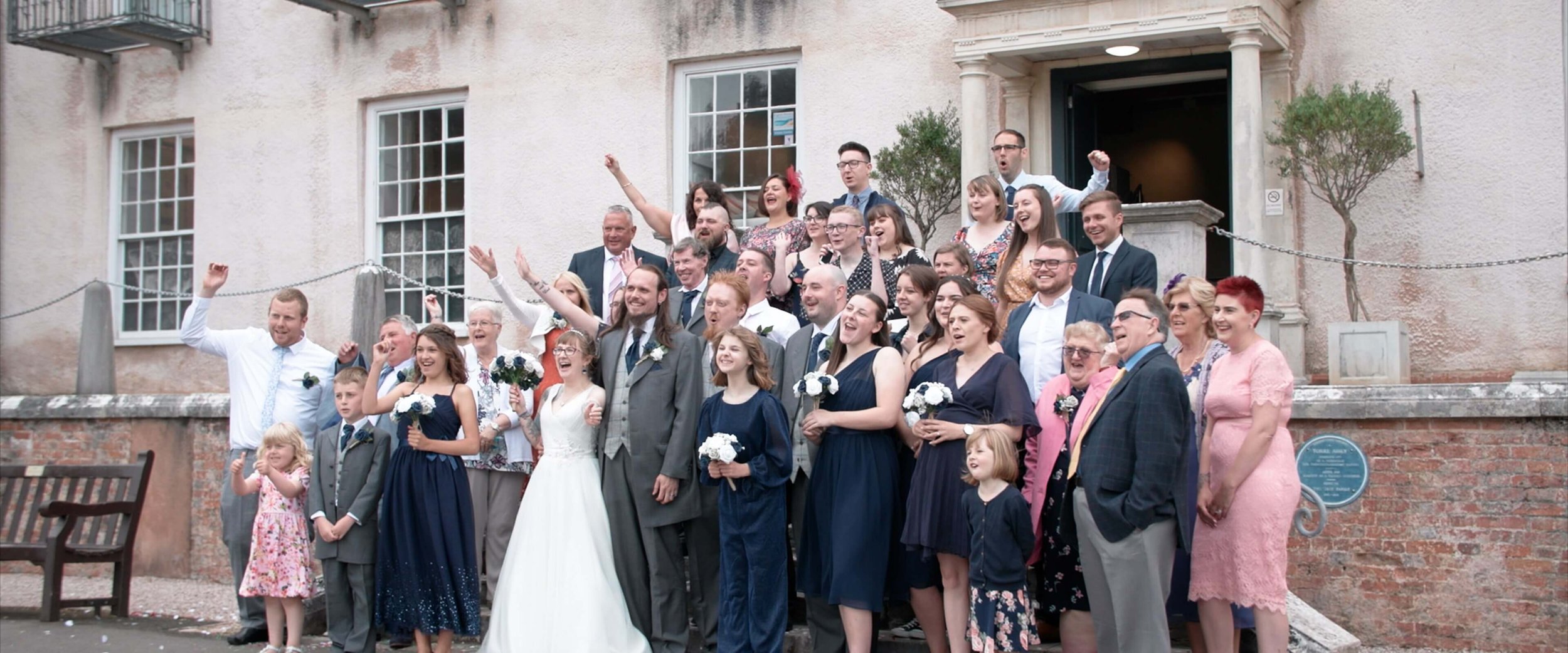 The entire wedding party cheer for a group photo in front of Torre Abbey