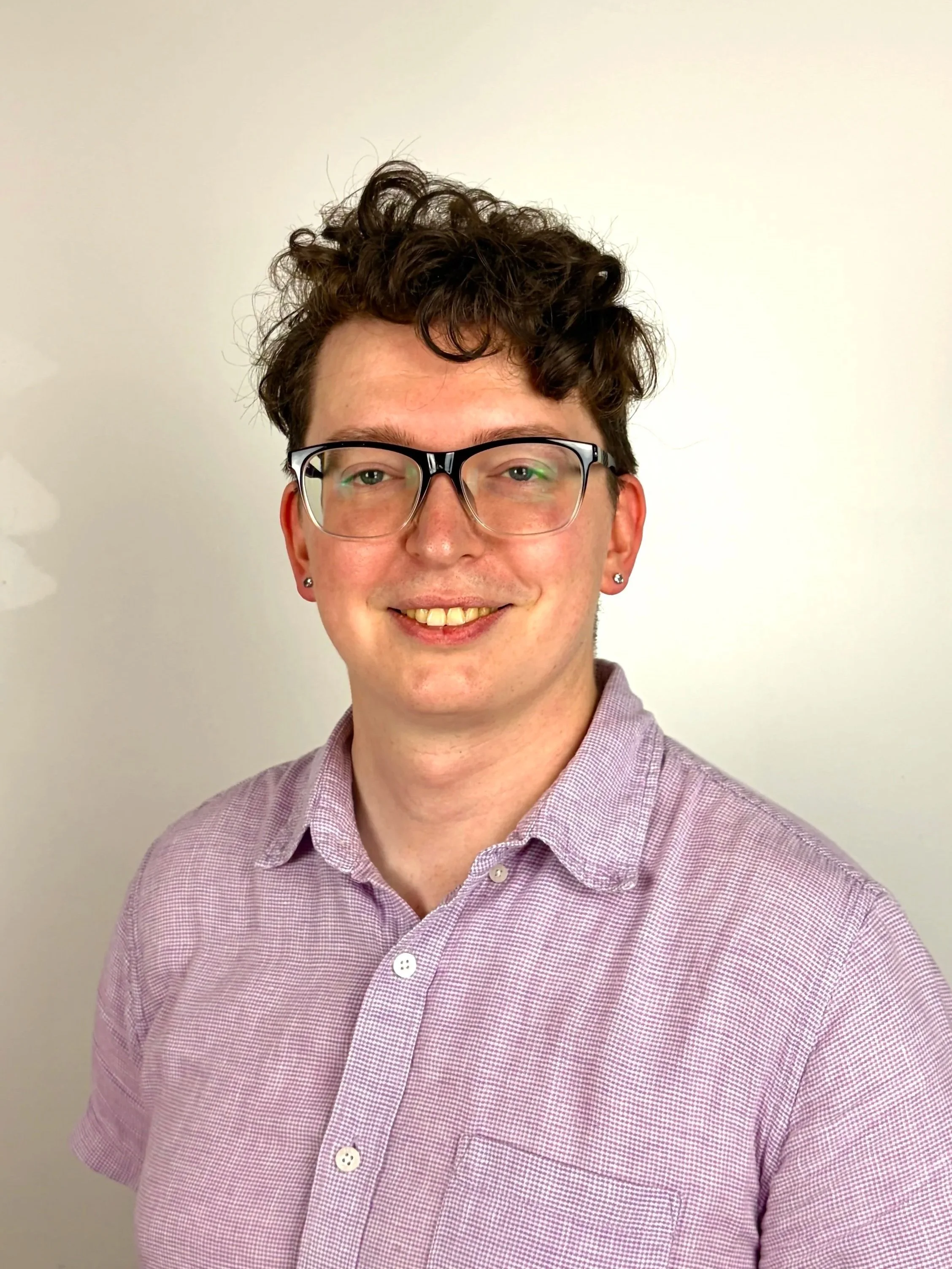 Young man with curly hair and glasses and a purple button up shirt smiling