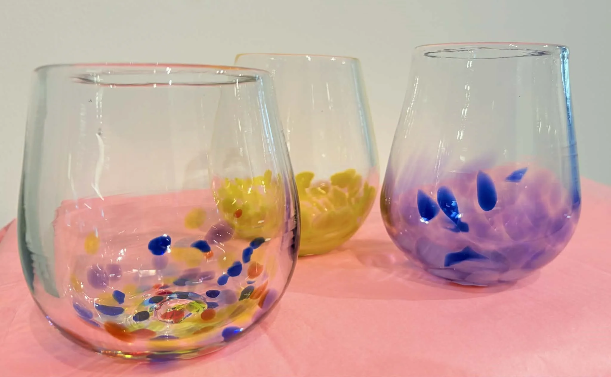 Three multicolored stemless wine glasses on a pink pedestal.