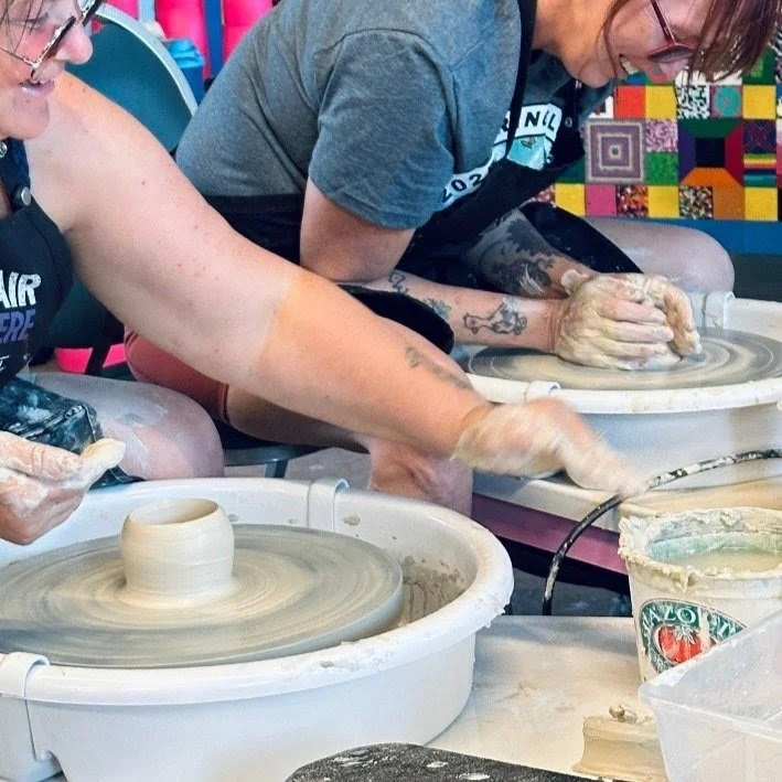 two adults making ceramic vessels on a ceramic wheel