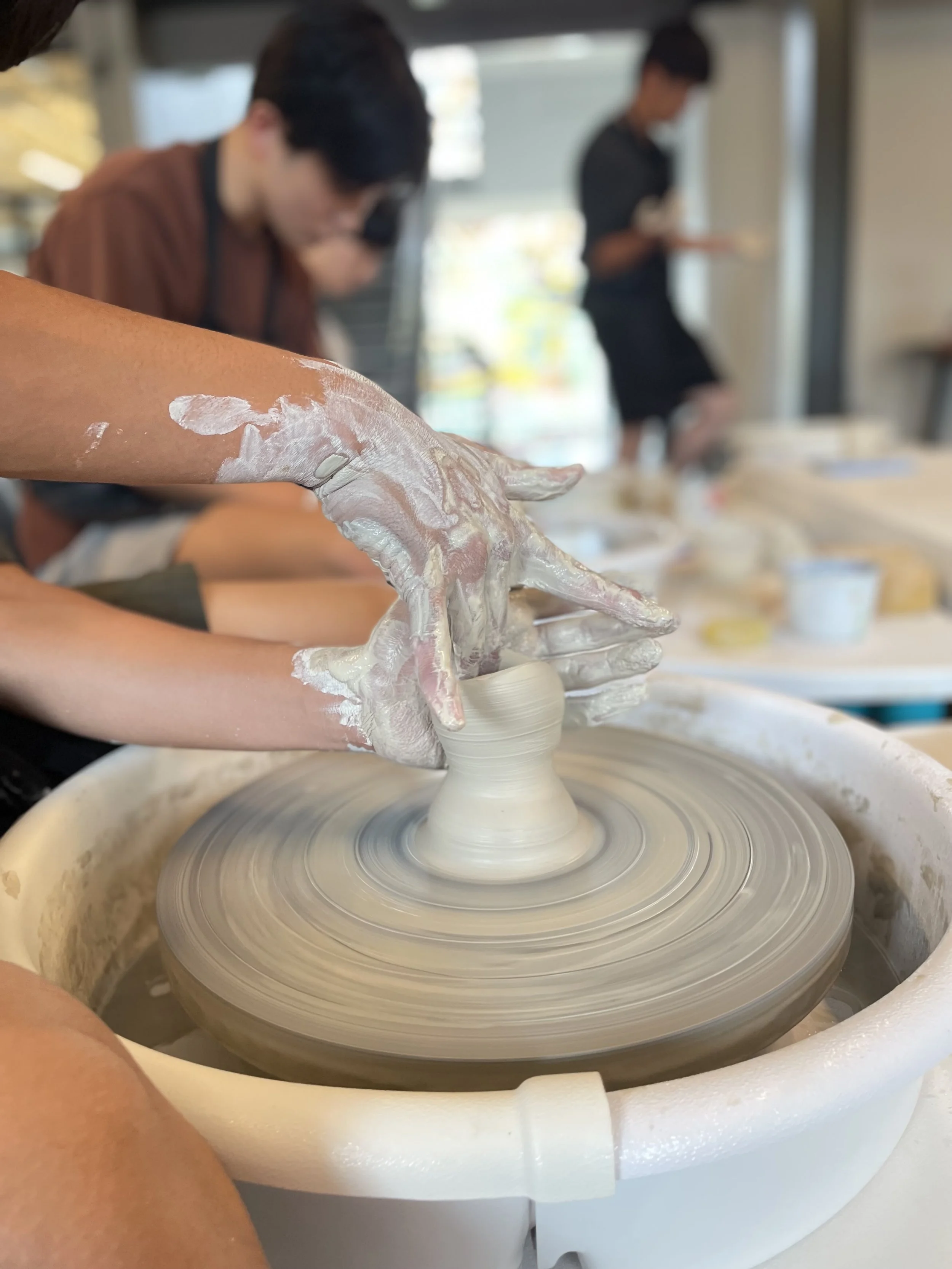 a set of hands sculpting clay on a ceramic wheel