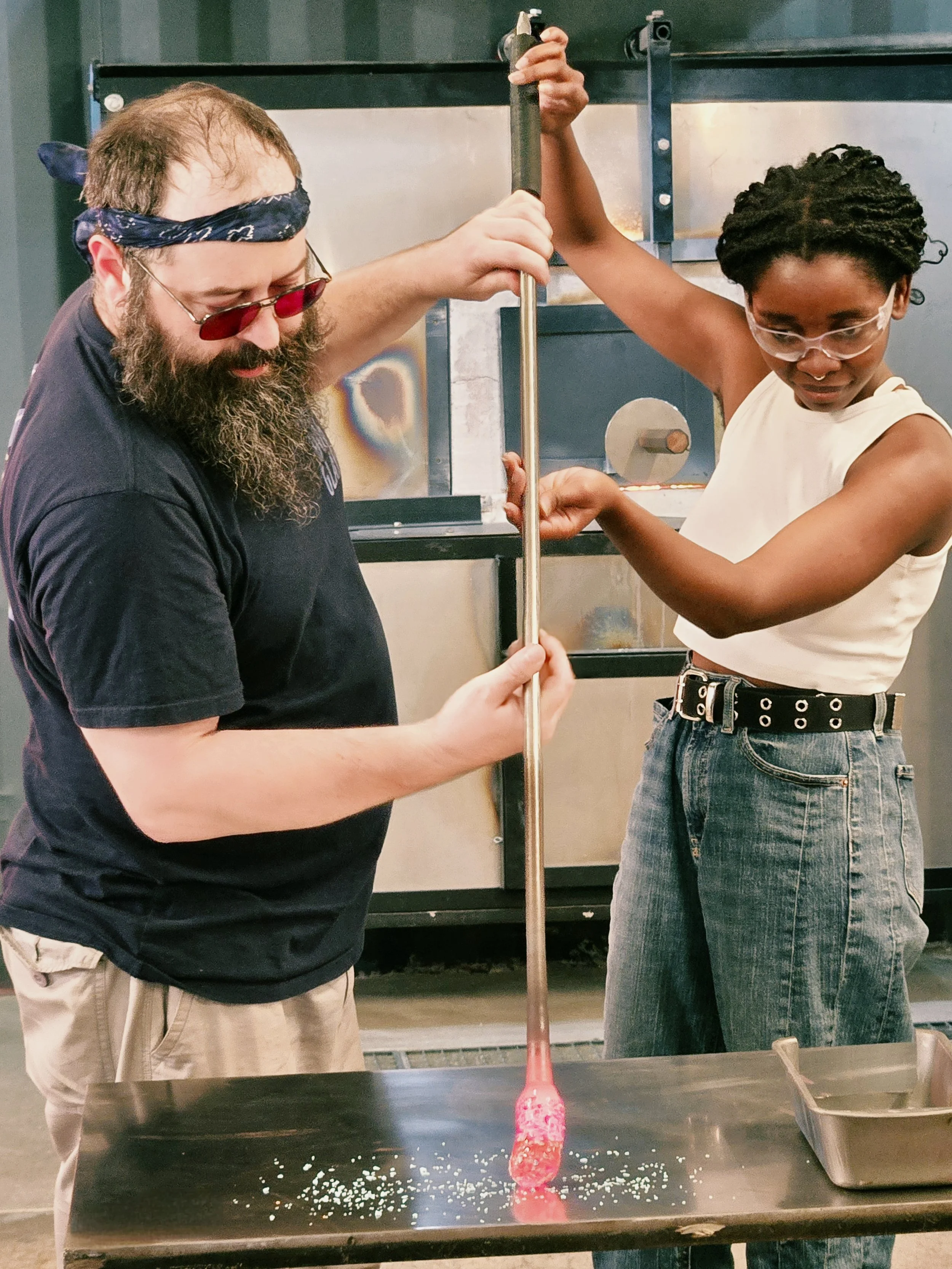 an instructor and student turning a glassblowing punty in color frit