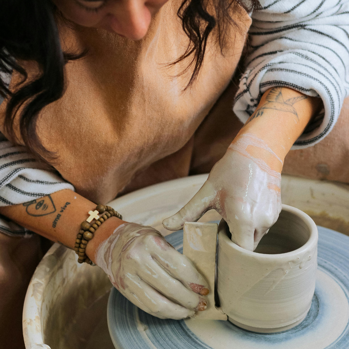 a woman using a ceramic wheel and tools to trim a clay vessel
