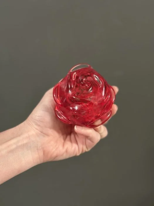 A hand holding a red rose made of glass.