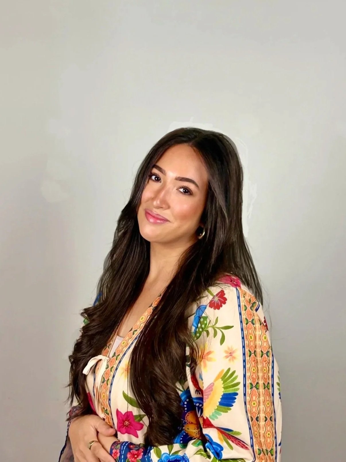 Young woman with long brown hair smiling in a patterned shirt