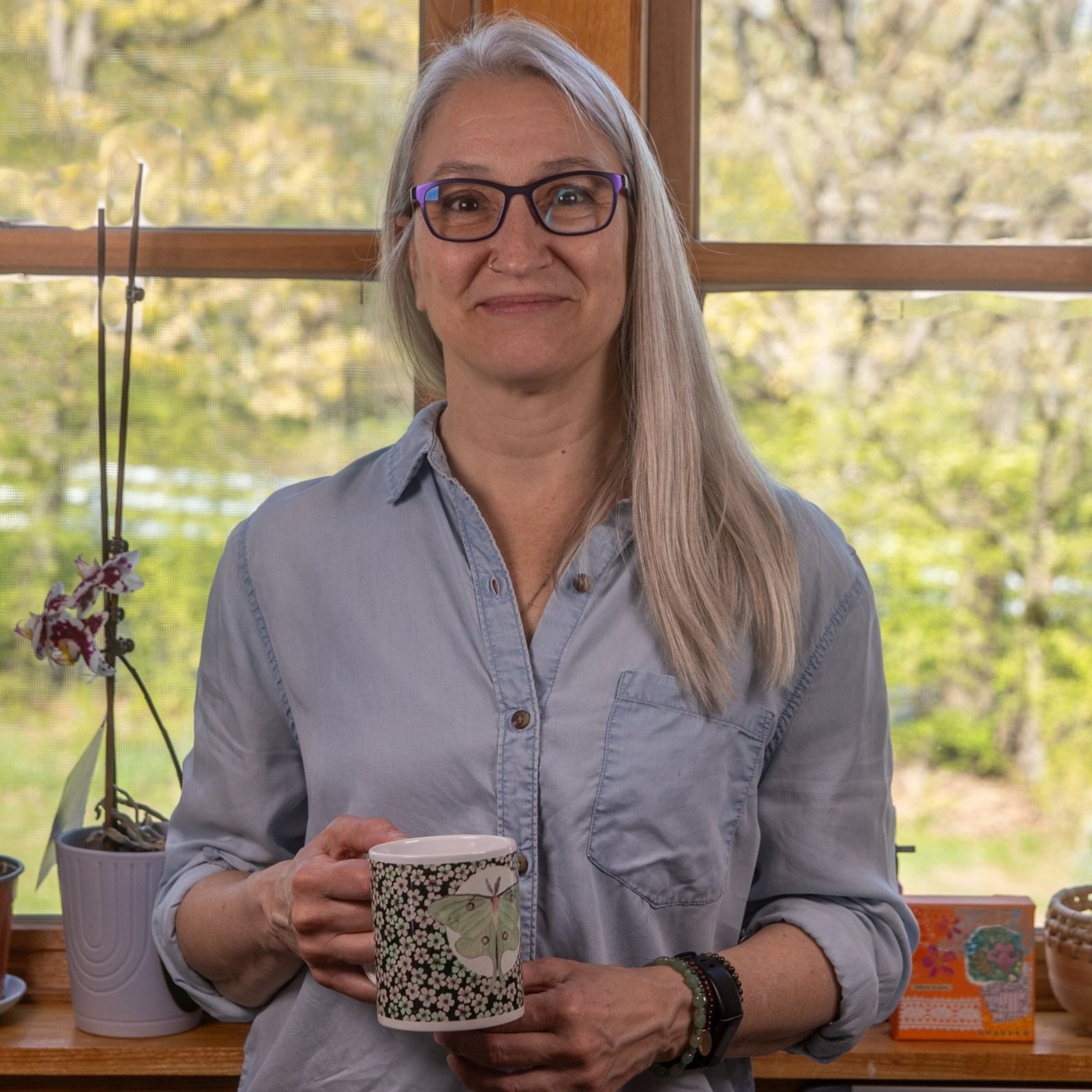 Photo of Janet Hild of Ink+Sun holding a mug with her Luna Moth art print printed on it.