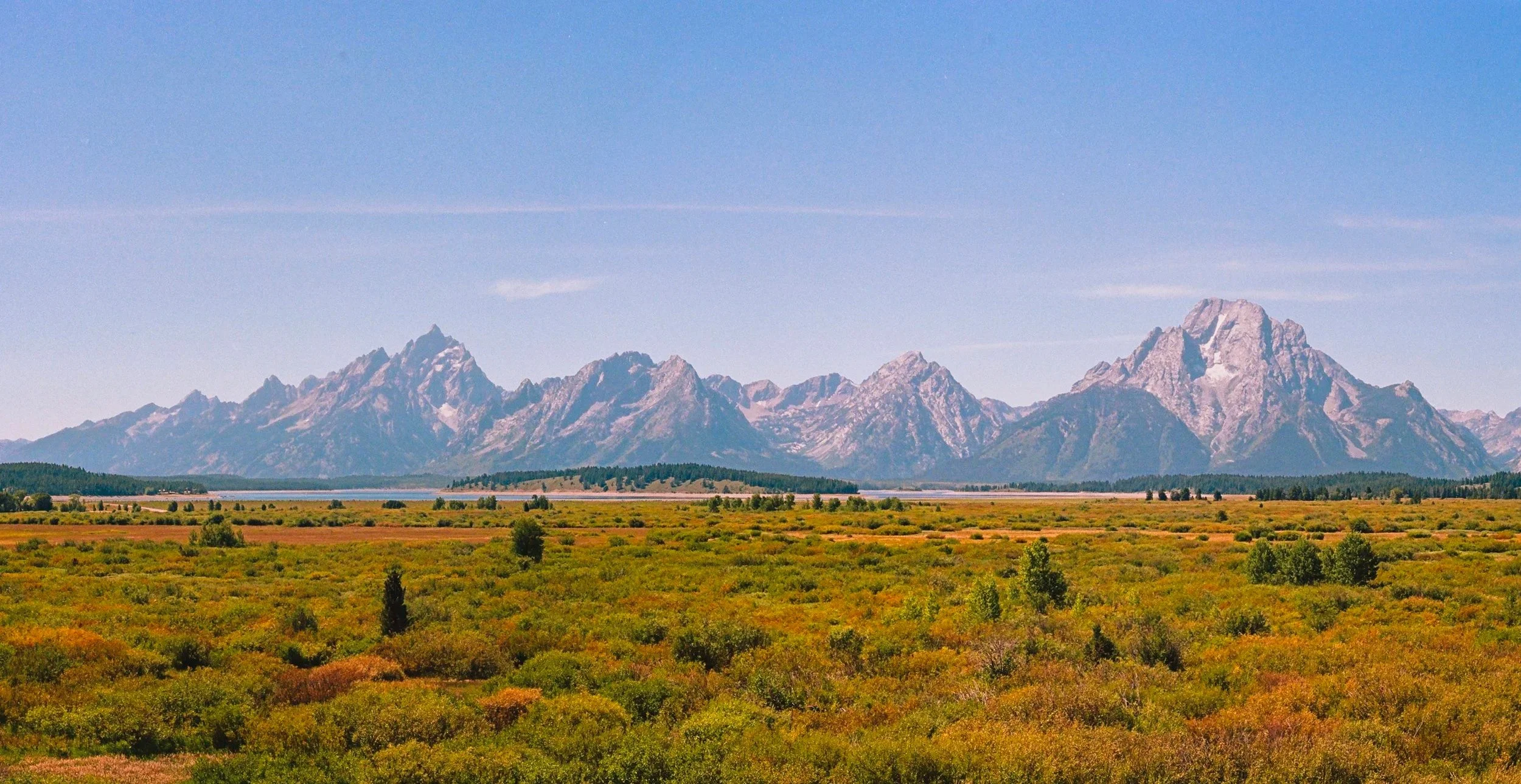 Scenic view of a mountain range with a grassy plain in the foreground and a clear blue sky above.