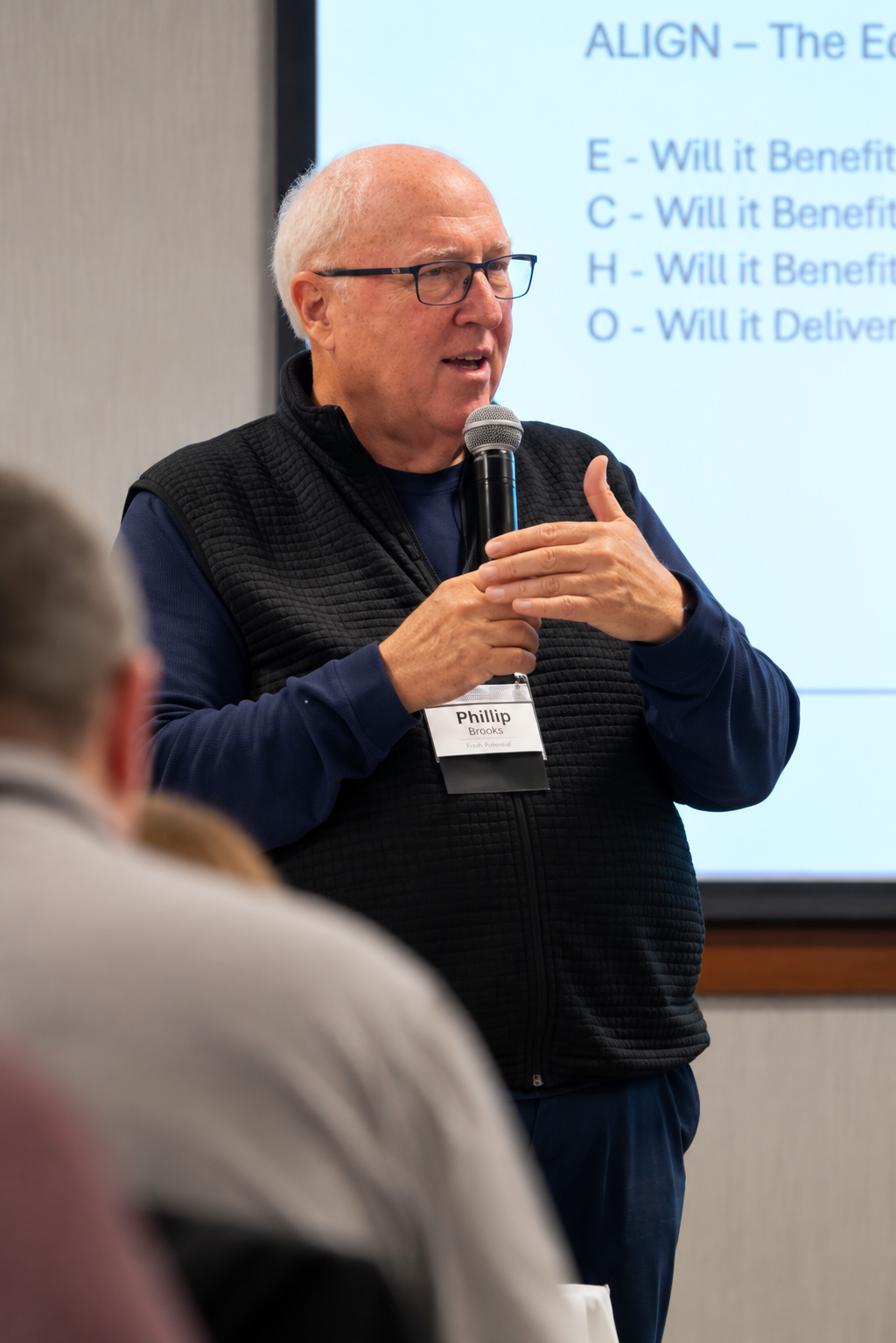 Phillip Brooks speaking to an audience, holding a microphone and gesturing beside an ECHO leadership slide.