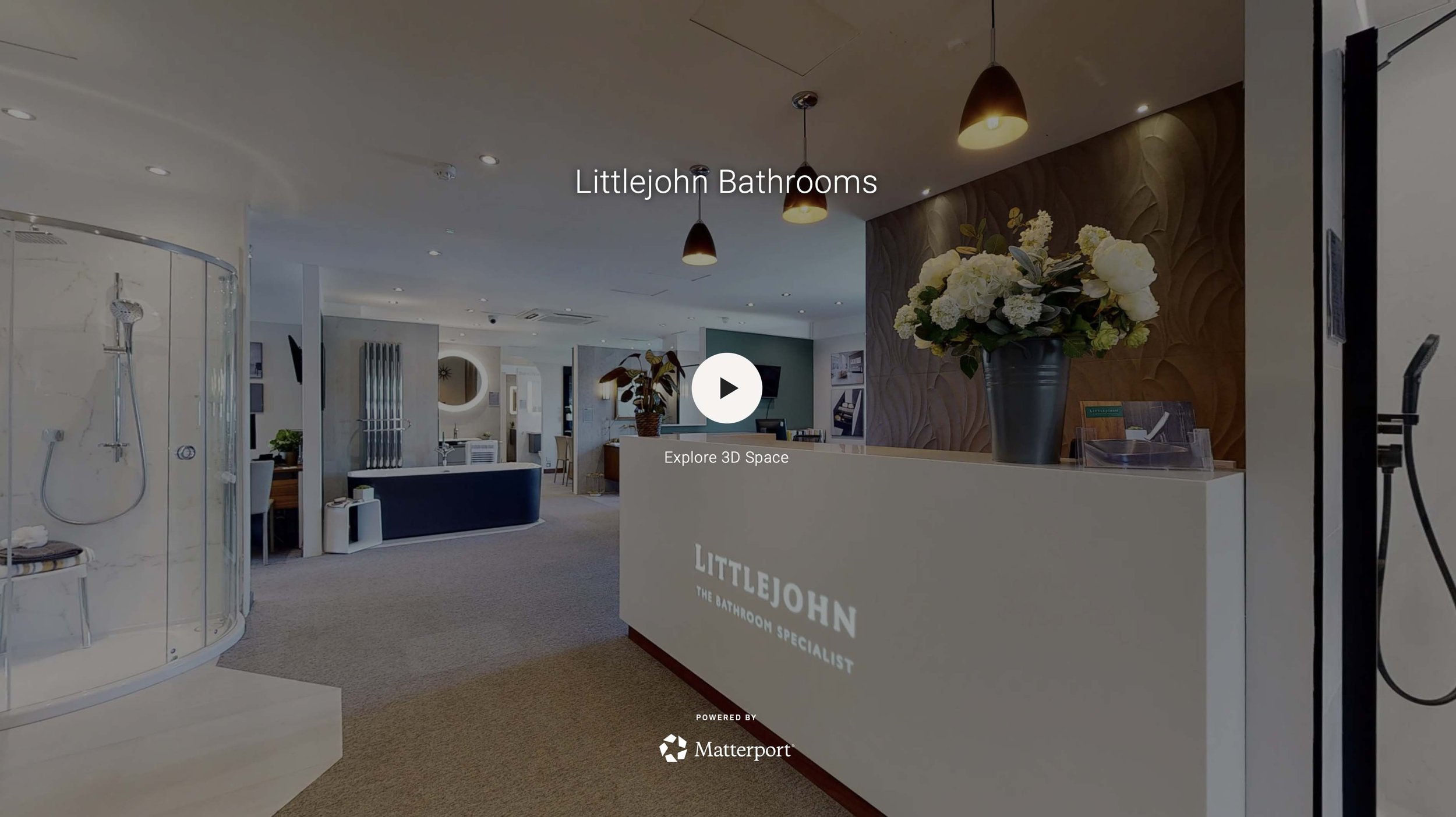 Interior of Littlejohn Bathrooms showroom with a reception desk, flowers, and a shower enclosure on the left.