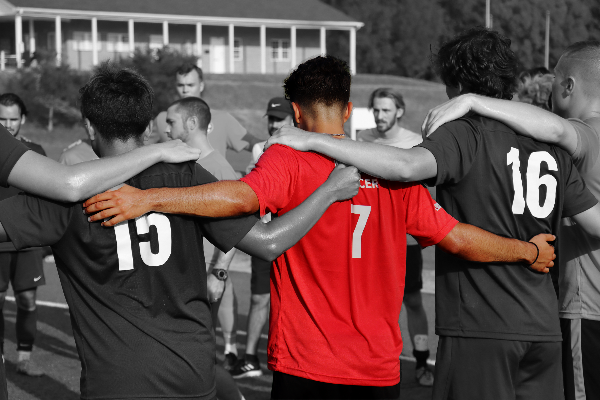 A soccer team huddles together with arms around each other, some in color and others in black and white.