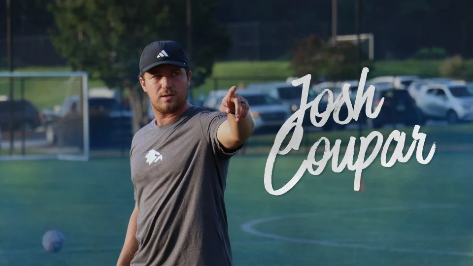 A man in a gray shirt and black cap on a soccer field, pointing towards the camera with the name 'Josh Coupar' written in stylized script.