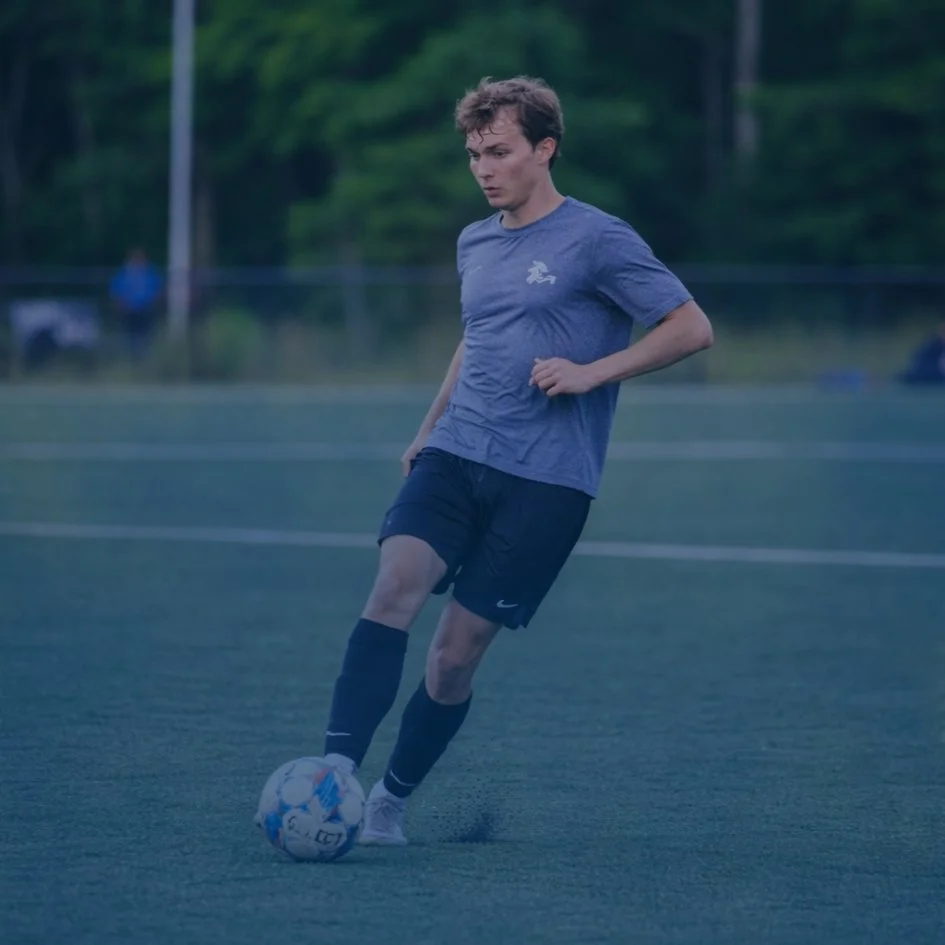 A young man in athletic clothes is on a soccer field, preparing to kick a soccer ball.