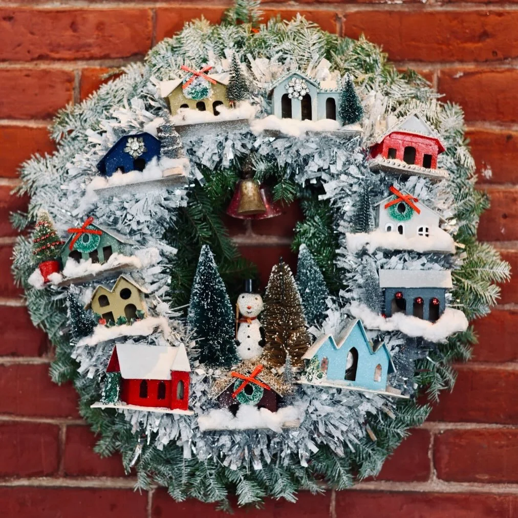 A tiny winter village has come to life. This year&rsquo;s Festival of Trees wreath from @frost.antiques features a mix of new and vintage Putz houses, snowy bottle-brush trees, and a charming vintage snowman tucked into the scene. Full of glow, nosta