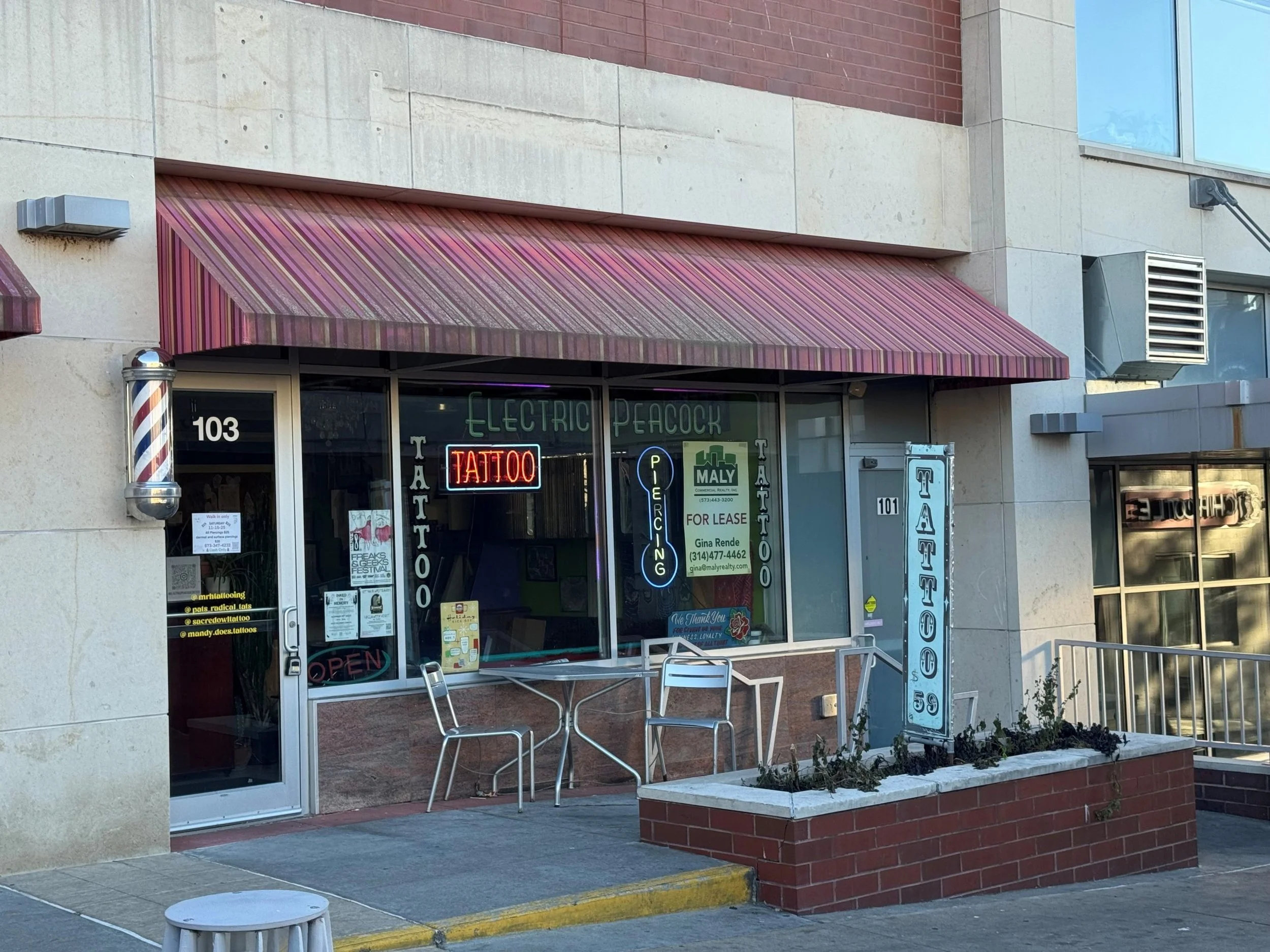 A storefront that says tattoo with a table and chairs out front.