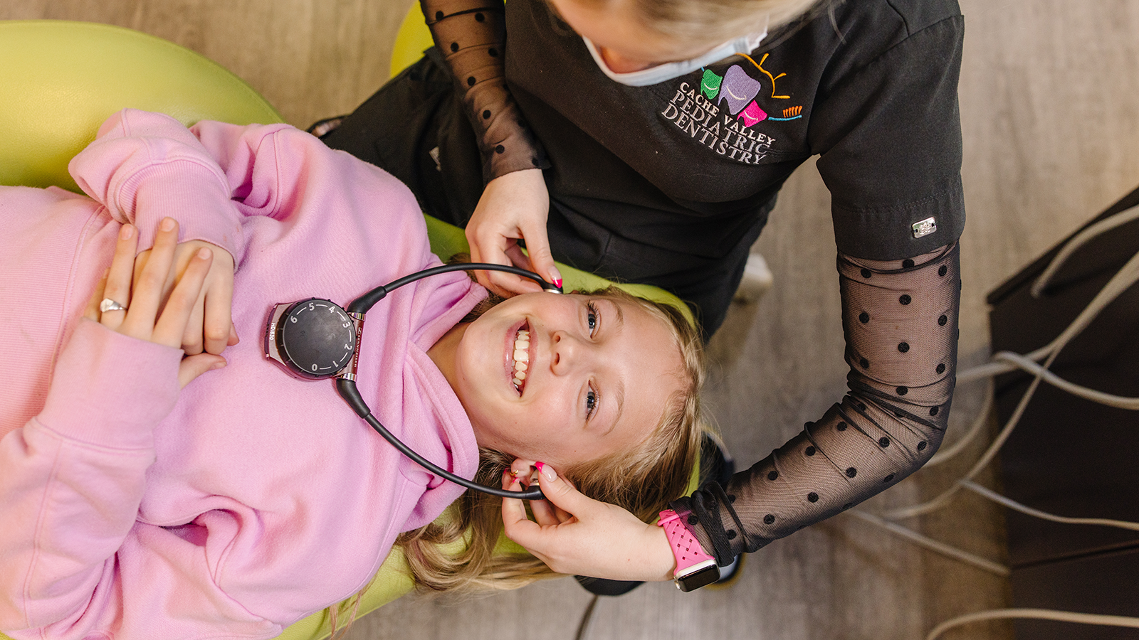 Happy young girl smiling as she lays in a chair at the dental office with the dental hygienist putting headphones on her