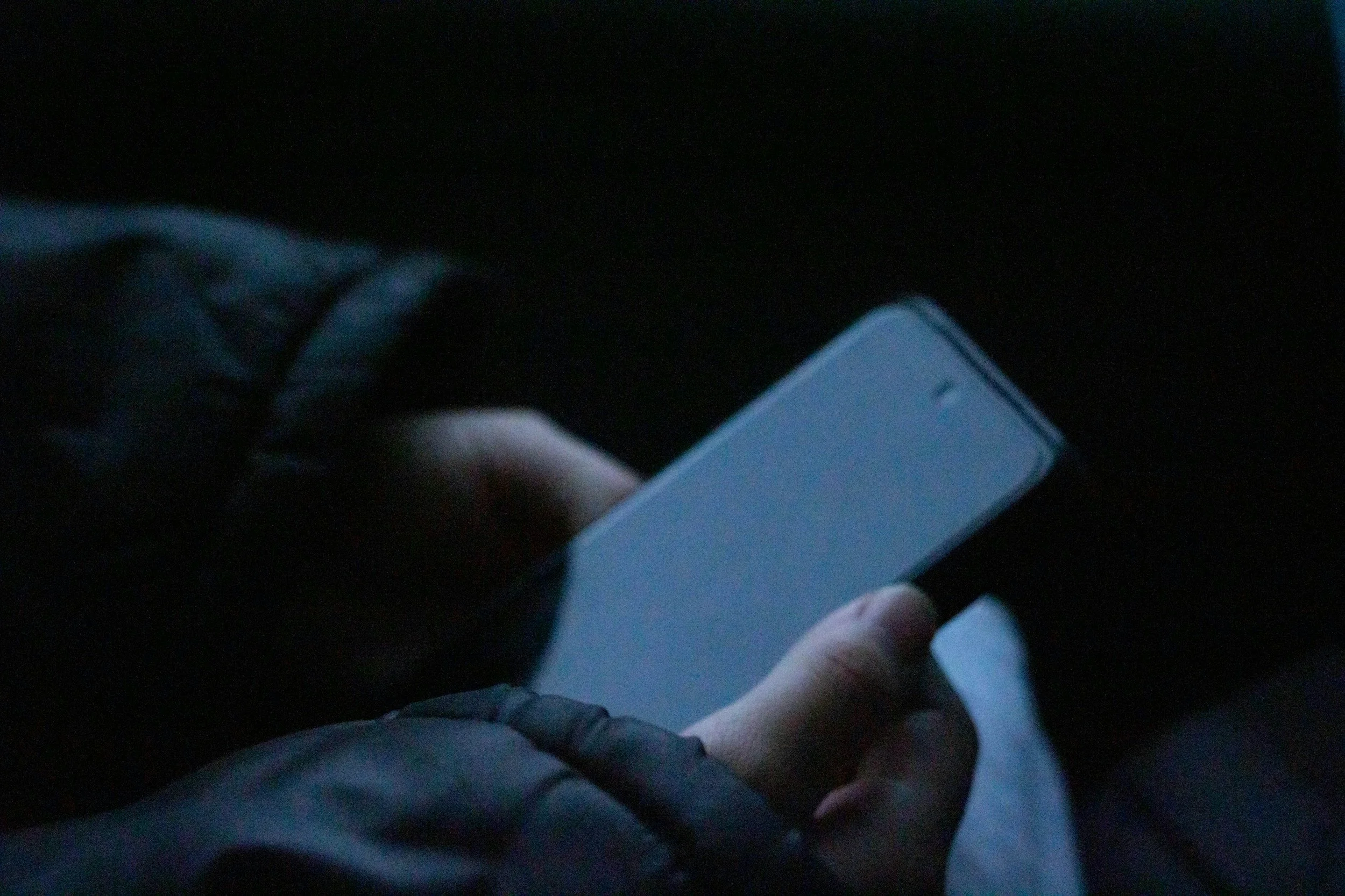 Person holding a smartphone in dark lighting.