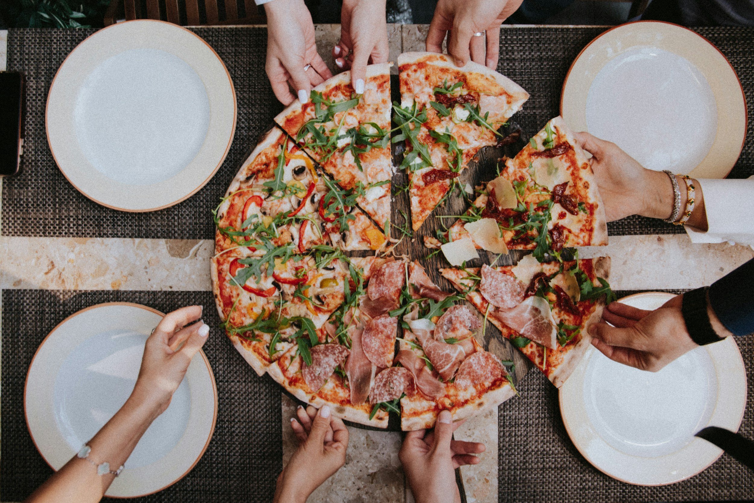 People sharing a large pizza with various toppings at a dining table, with empty plates around.