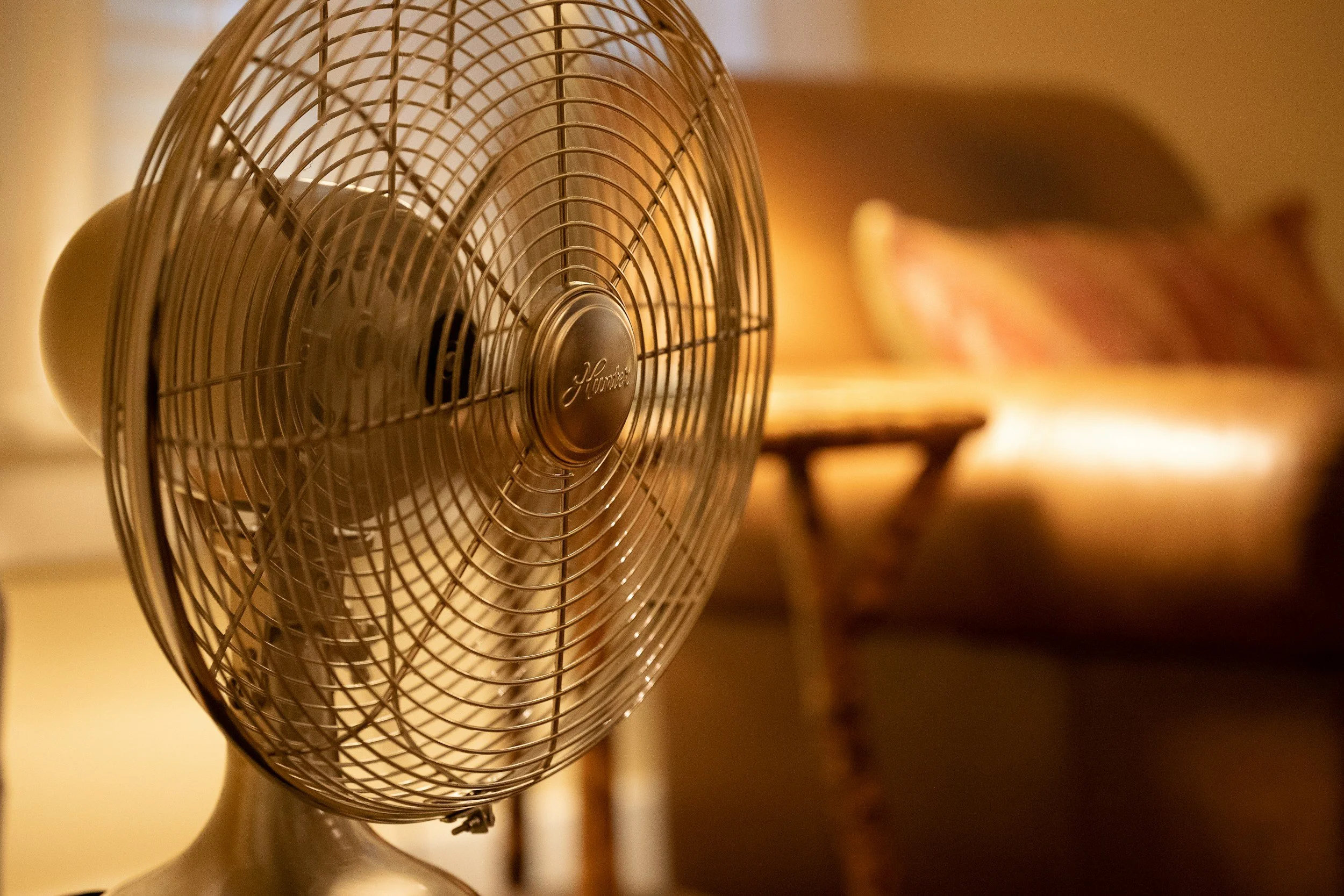 An oscillating fan in a warm-lit room with a sofa and a small table in the background.