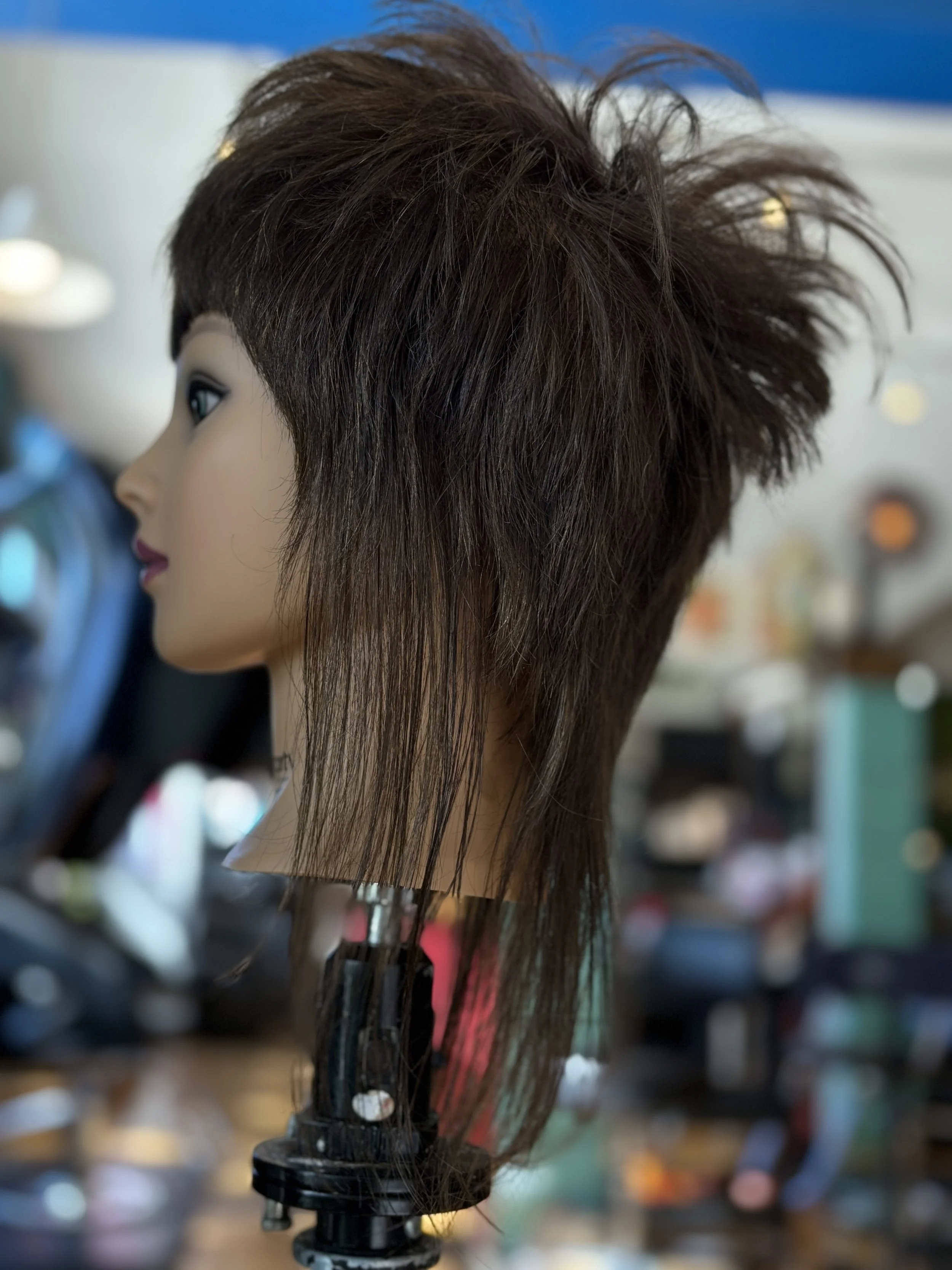 A mannequin head with a brown, spiked, layered hairstyle, set on a stand in a beauty salon or barber shop.