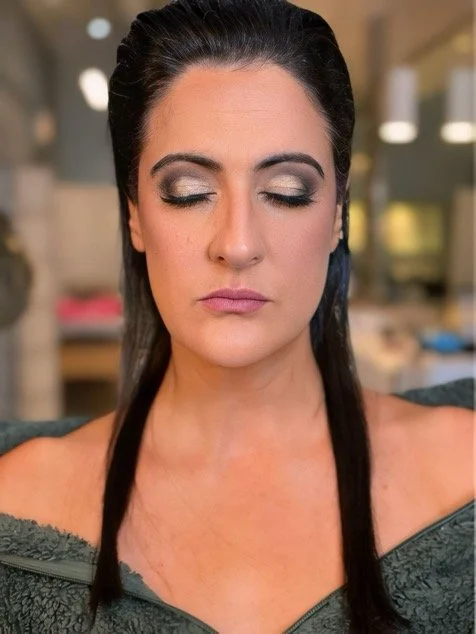 A woman with closed eyes, dark hair pulled back, and makeup including silver eyeshadow and lipstick.