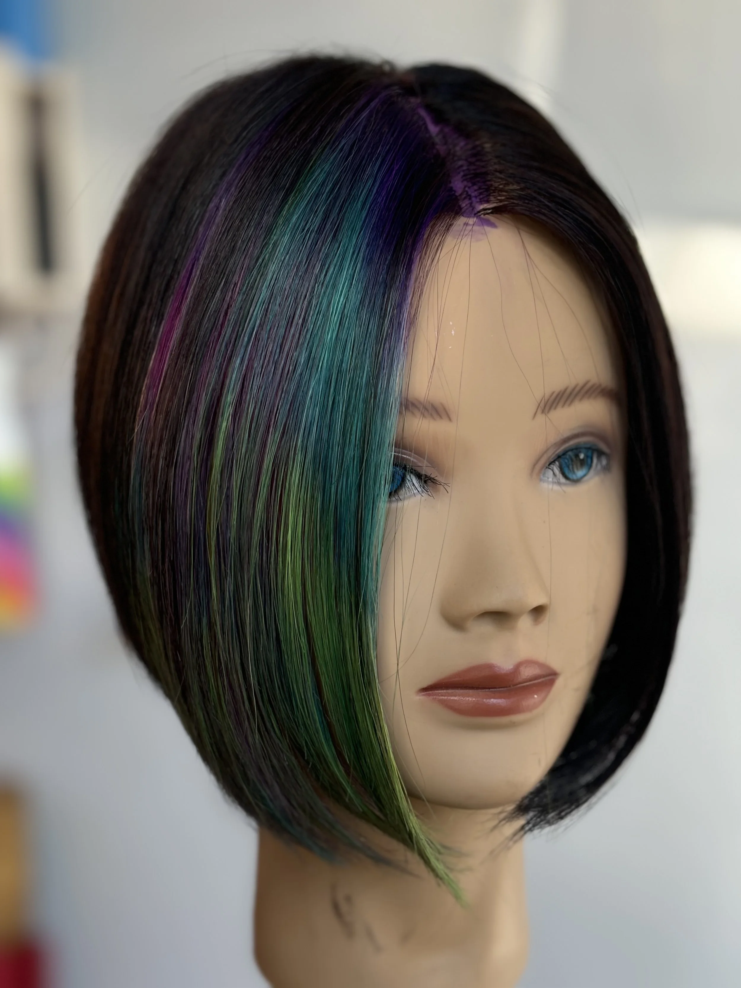 A mannequin head with a short, asymmetrical haircut dyed with shades of purple, blue, and green.