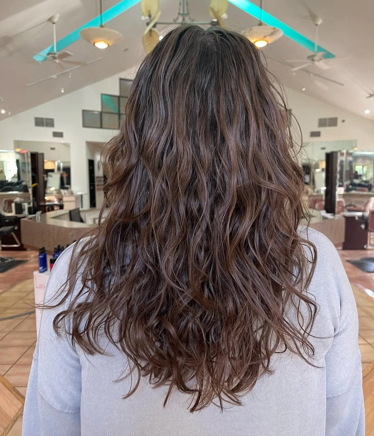 Back of a woman with long, curly, brown hair inside a hair salon.