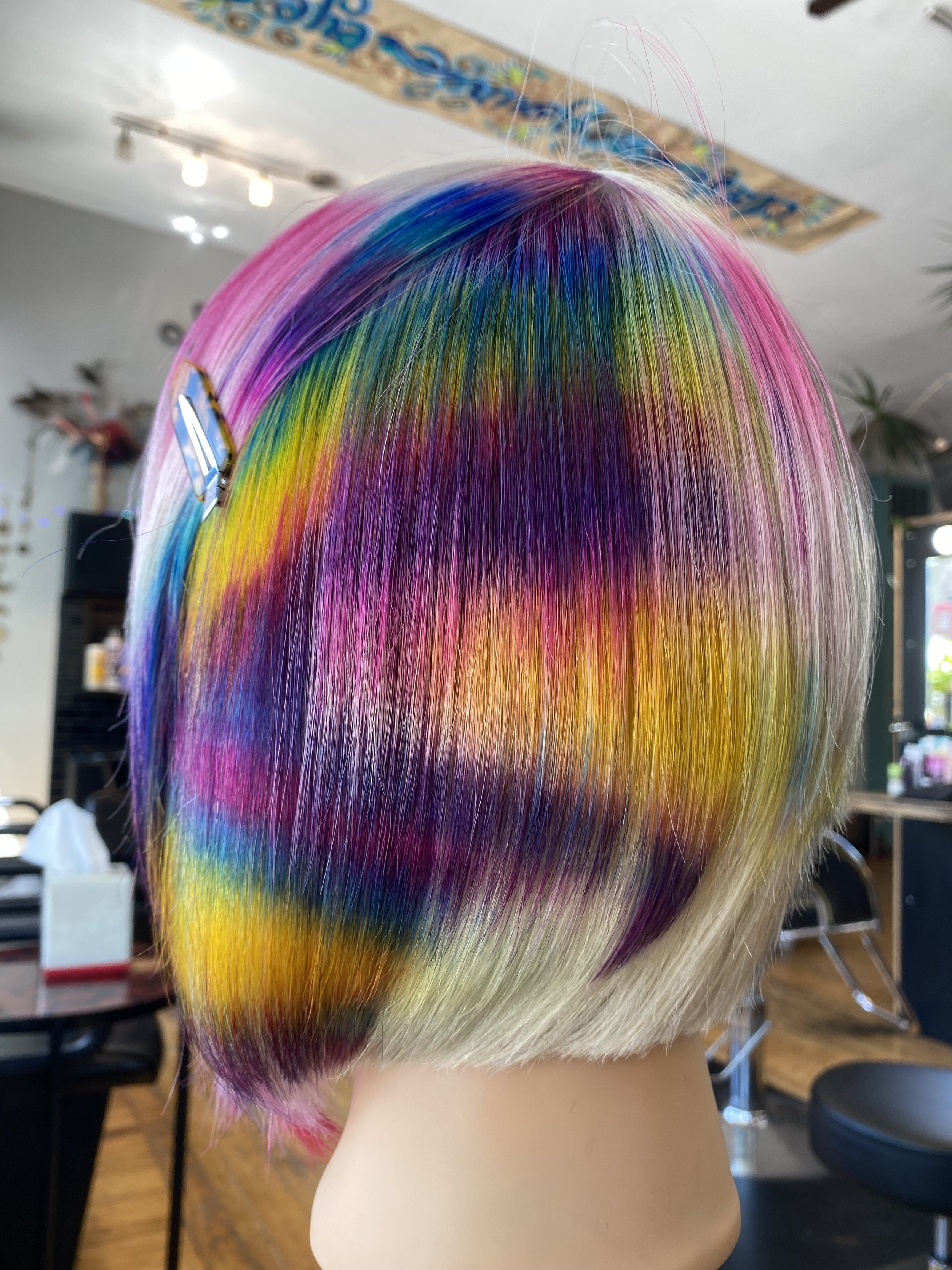 A mannequin head with straight, shoulder-length, multicolored hair in a salon setting.