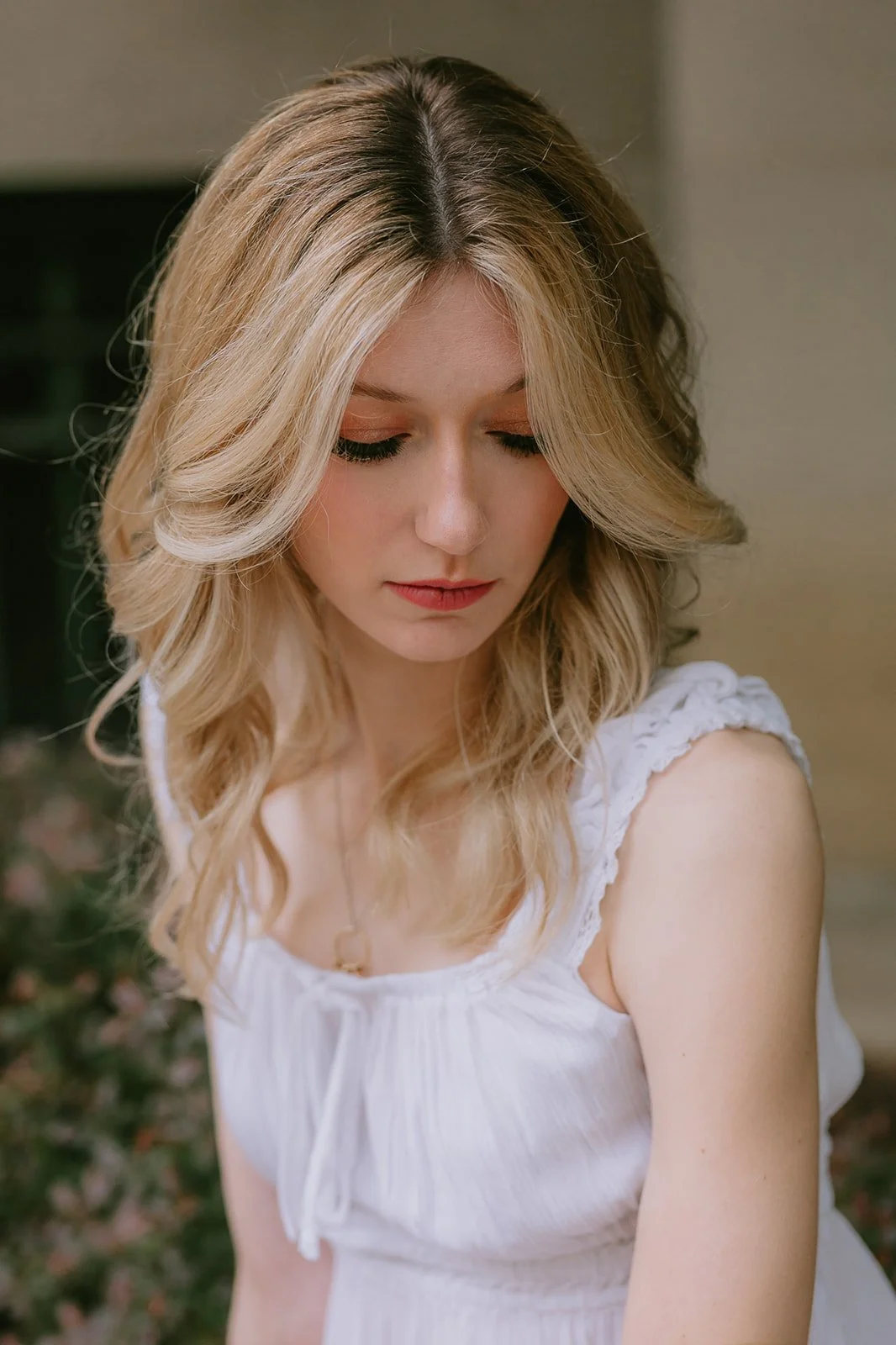 A woman with blonde hair and a white sleeveless top looking down.