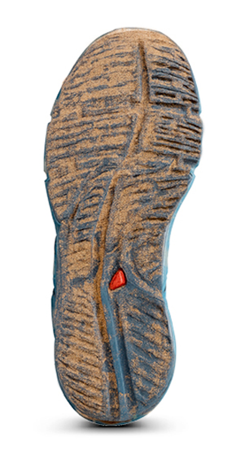 Semelle de chaussure avec crampons en caoutchouc, vue de dessous, avec une petite pièce rouge.