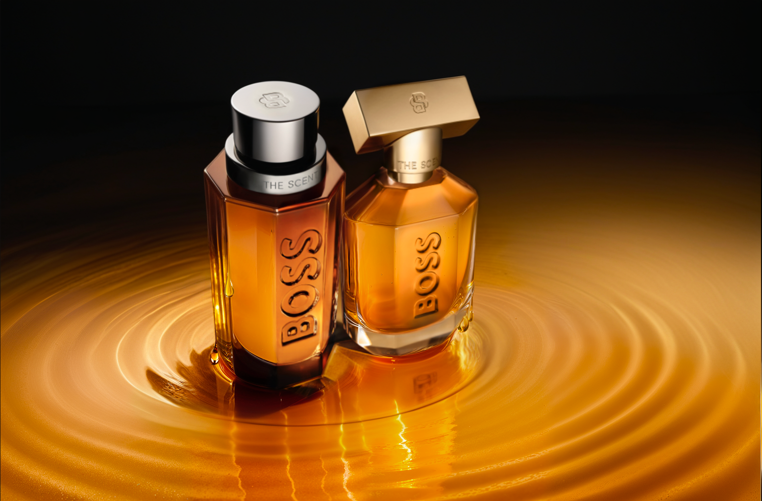Deux flacons de parfum Hugo Boss, un en forme rectangulaire avec capuchon argenté et un autre plus petit avec un capuchon or, reposant sur une surface dorée avec un effet de cercle concentrique lumineux.