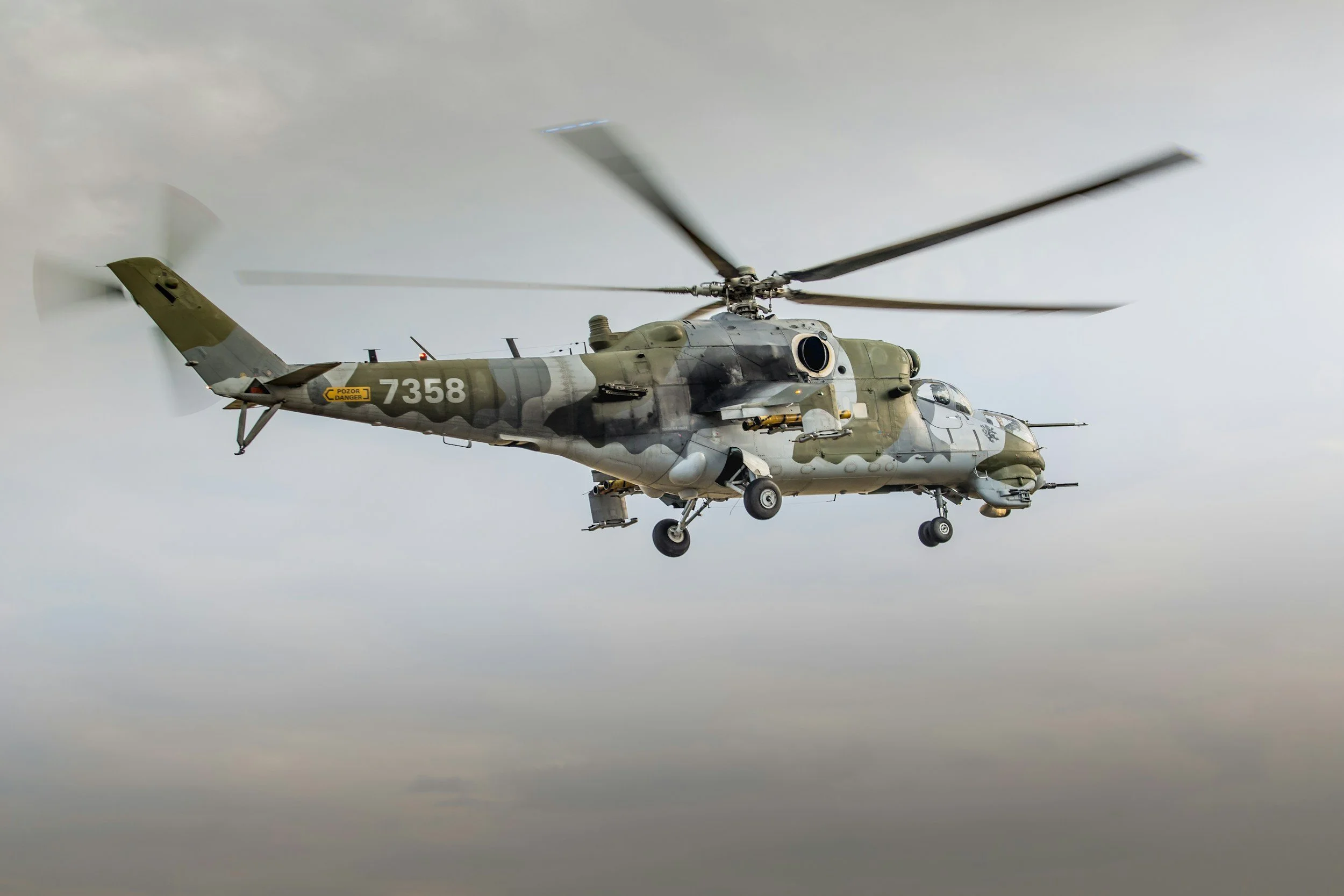 Military helicopter flying in the sky with a camouflage pattern and the number 7358 on its side.