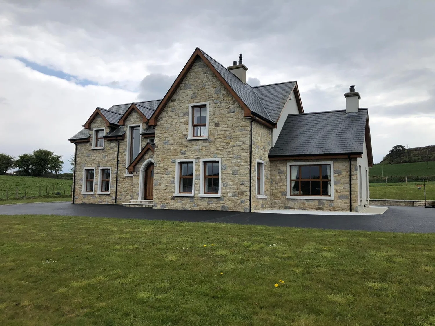 Detached home with natural sandstone walls, gabled slate roofs and pale stone window surrounds