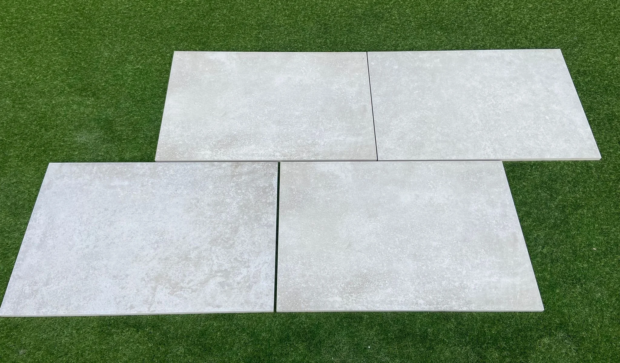 Image of a Portuguese White Porcelain as supplied by Shanlieve Stone from their  yard in Newry where they have their paving range displayed. The image shows 4 slabs of the Portuguese white porcelain on grass