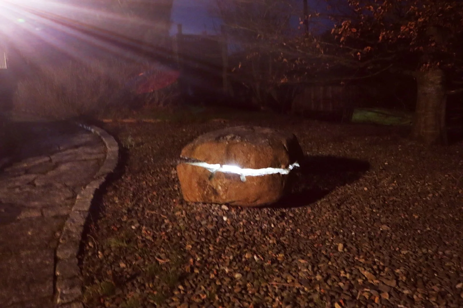 Image shows a large granite boulder split in two with a light placed in the centre allowing light to flow through the cracks on the stone creating a unique natural stone garden feature 