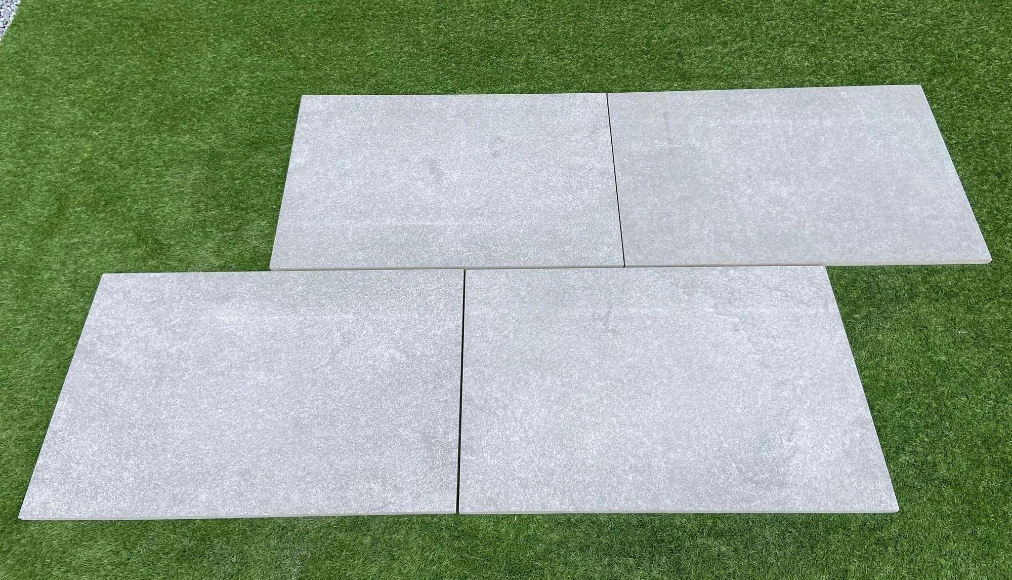Image is of a Portuguese Grey Porcelain. 4 slabs lying on grass in Shanlieve Stones display yard in Newry where they supply their porcelain products throughout Ireland