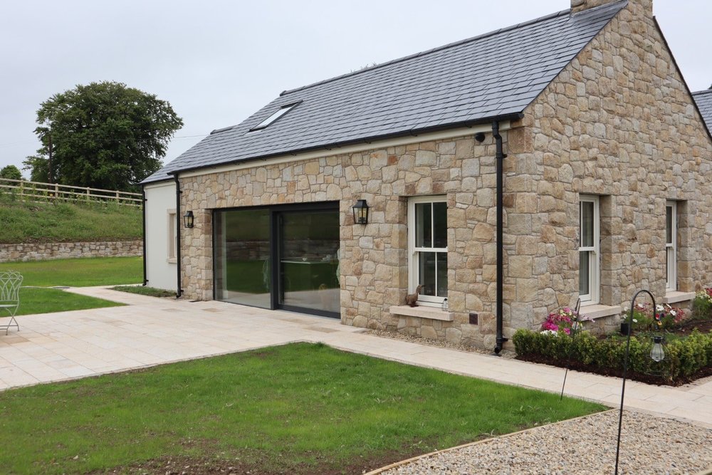 House with warm-toned natural building stone walls beside a lawn and patio